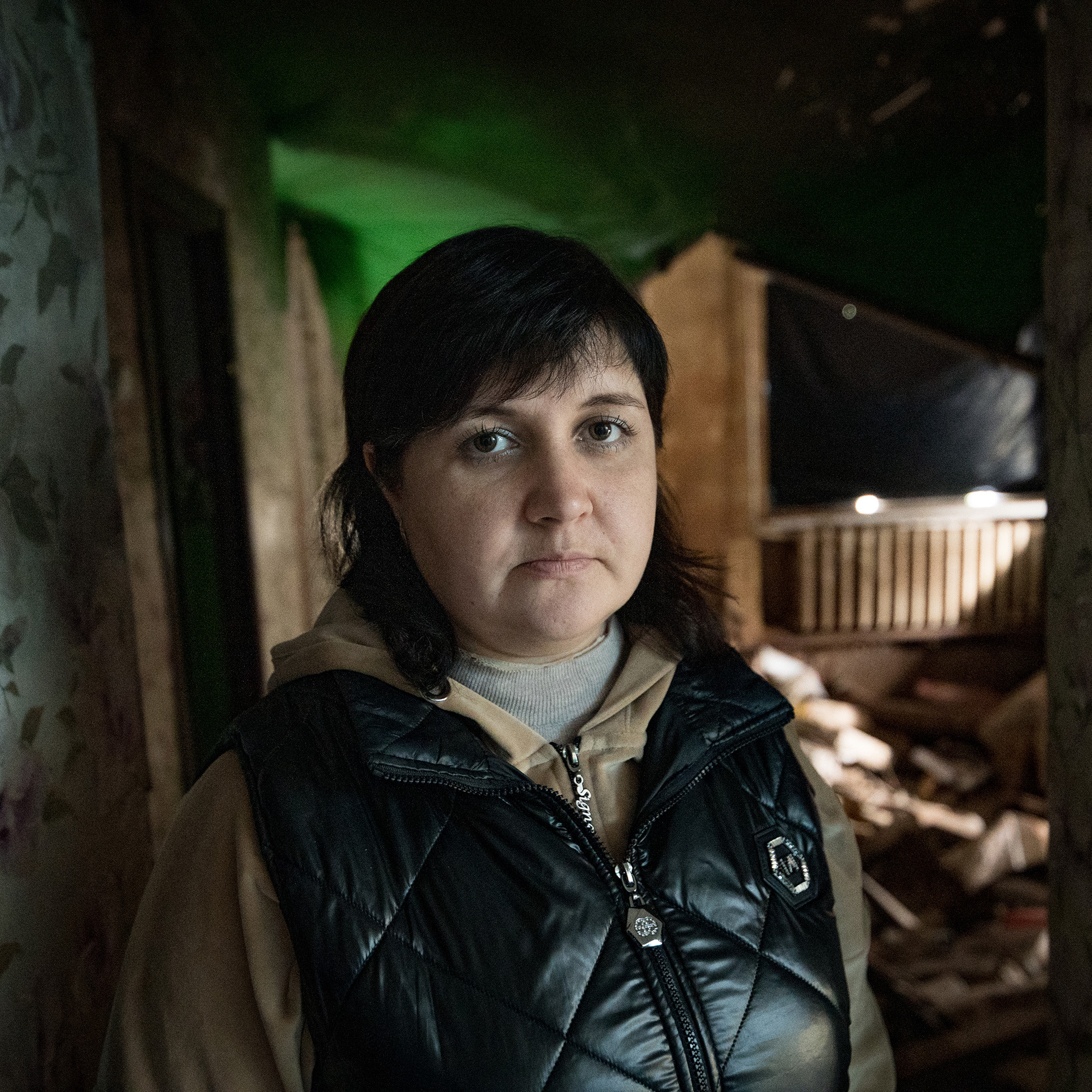 Eine Frau in Winterjacke steht in der Eingangstür einer zerstörten Wohnung und schaut in die Kamera.