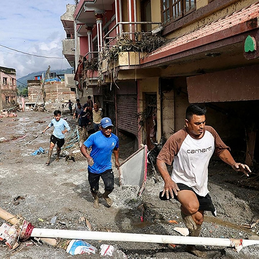 Einheimische gehen am 27. August 2026 in Devighat in der Stadt Bidur im nepalesischen Distrikt Nuwakot an Häusern vorbei, die nach Sturzfluten von Schlamm überschwemmt sind. Nach Angaben der nepalesischen Katastrophenschutzbehörde galten am 27. August noch 823 Menschen als vermisst, mehr als 24 Stunden nachdem eine tödliche Flut die Grenzregion zu Tibet heimgesucht hatte.