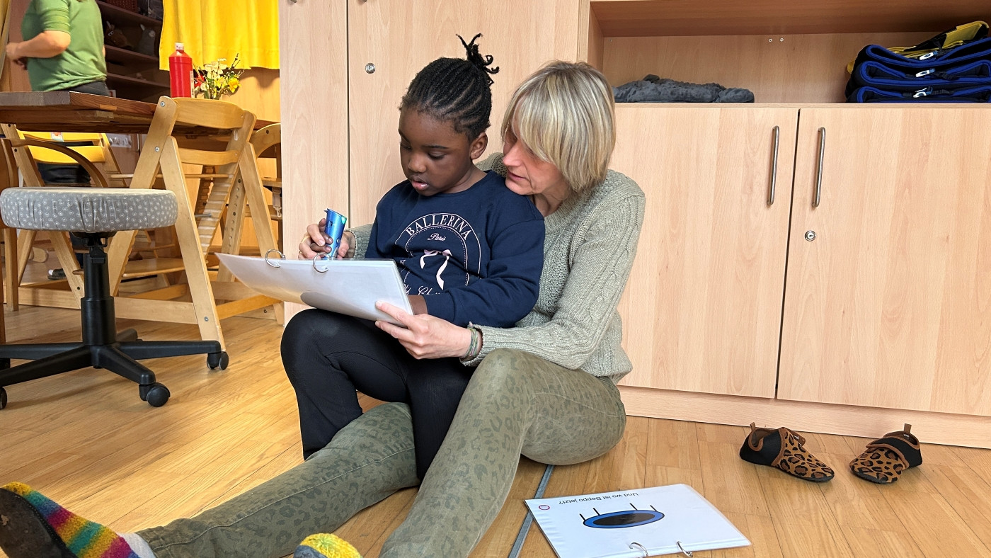 Kind sitzt auf Schoß von Dame, gemeinsam betrachten sie ein Dokument