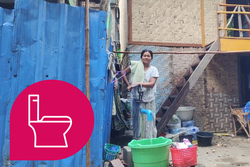 Frau pumpt Wasser in einen Eimer. Sie steht vor einem Haus aus Palmenblättern