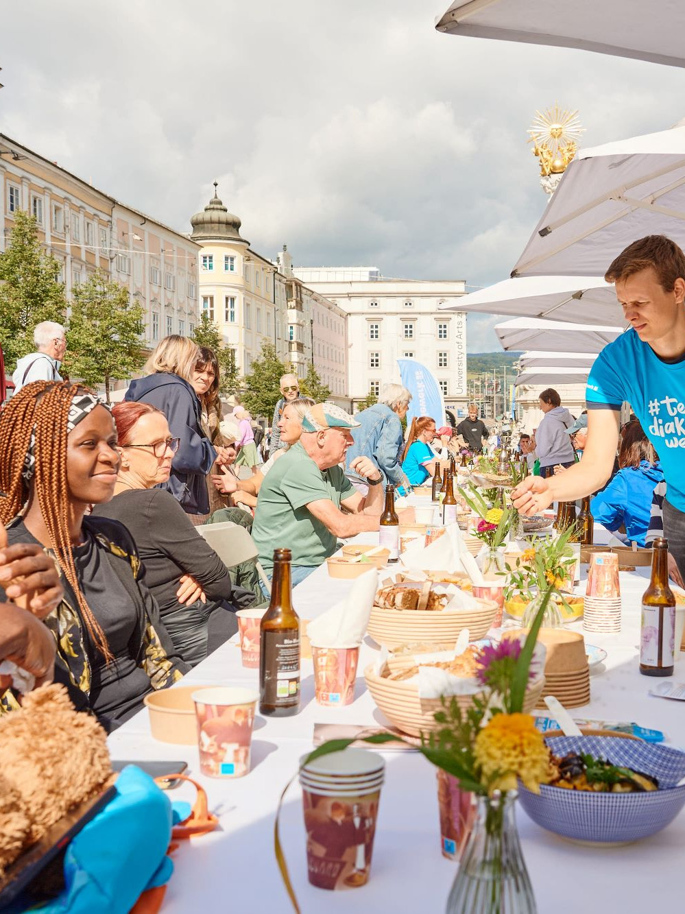 Unterschiedliche Personen sitzen an einer schön gedeckten Tafel und essen, trinken und plaudern
