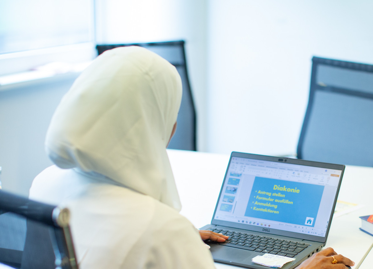 Junge Frau mit Kopftuch sitzt am Schriebtisch und schaut in ihren Laptop