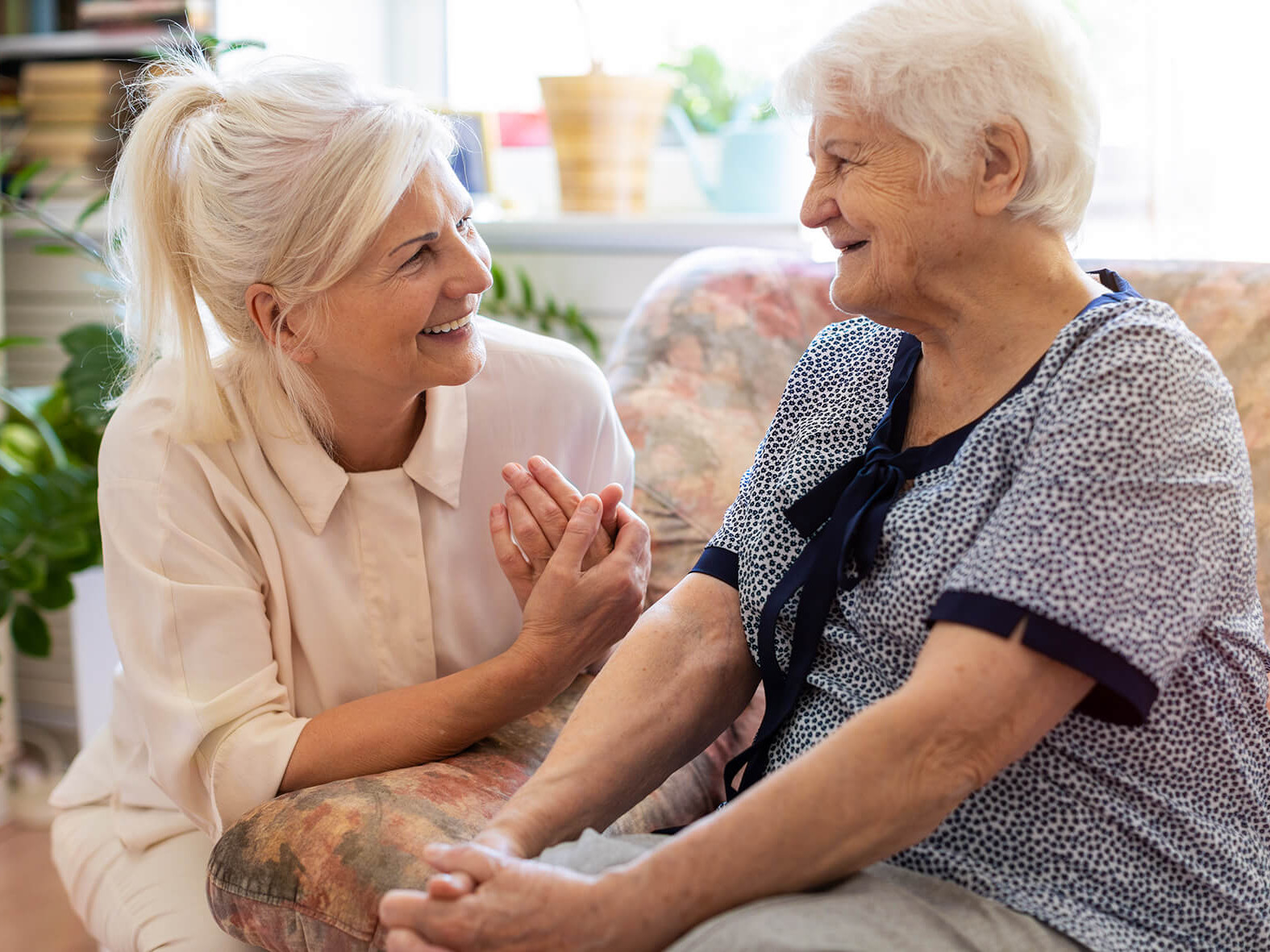 Zwei Frauen unterhalten sich und lächeln. Die ältere Frau sitzt auf der Couch.