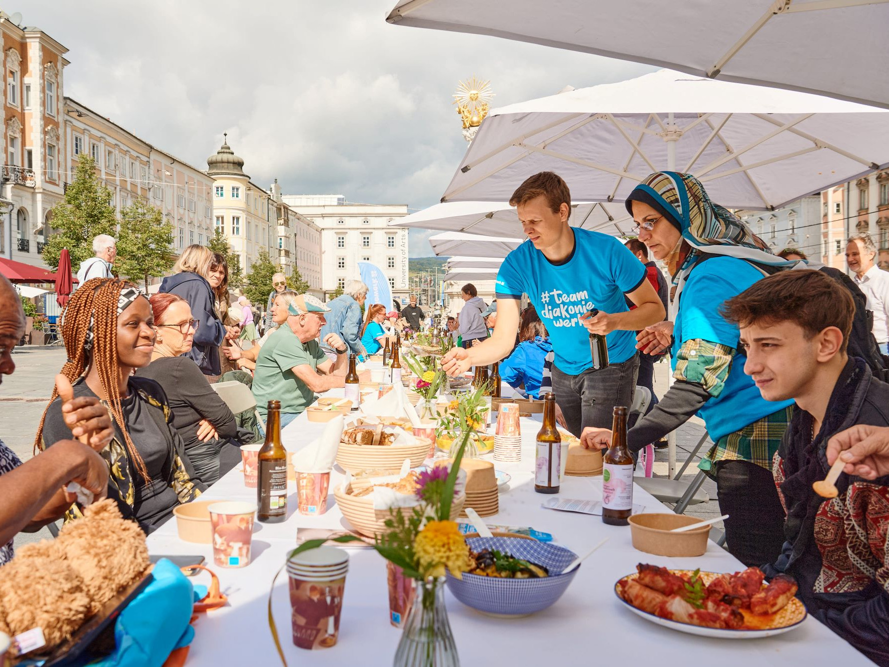 Unterschiedliche Personen sitzen an einer schön gedeckten Tafel und essen, trinken und plaudern