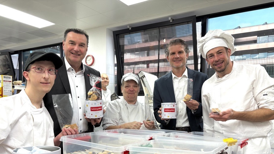 Andreas Gasteiger und Florian Schwap stehen  (Salzburg Milch) mit einem Fachmitarbeiter und KlientInnen des Kulinarium in einer Küche zusammen und halten Kekse und eine Keksdose in die Kamera.