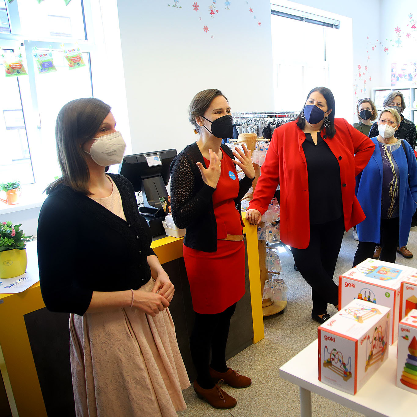 Eine Frau spricht vor zahlreichen Besucher:innen in einem Geschäft.