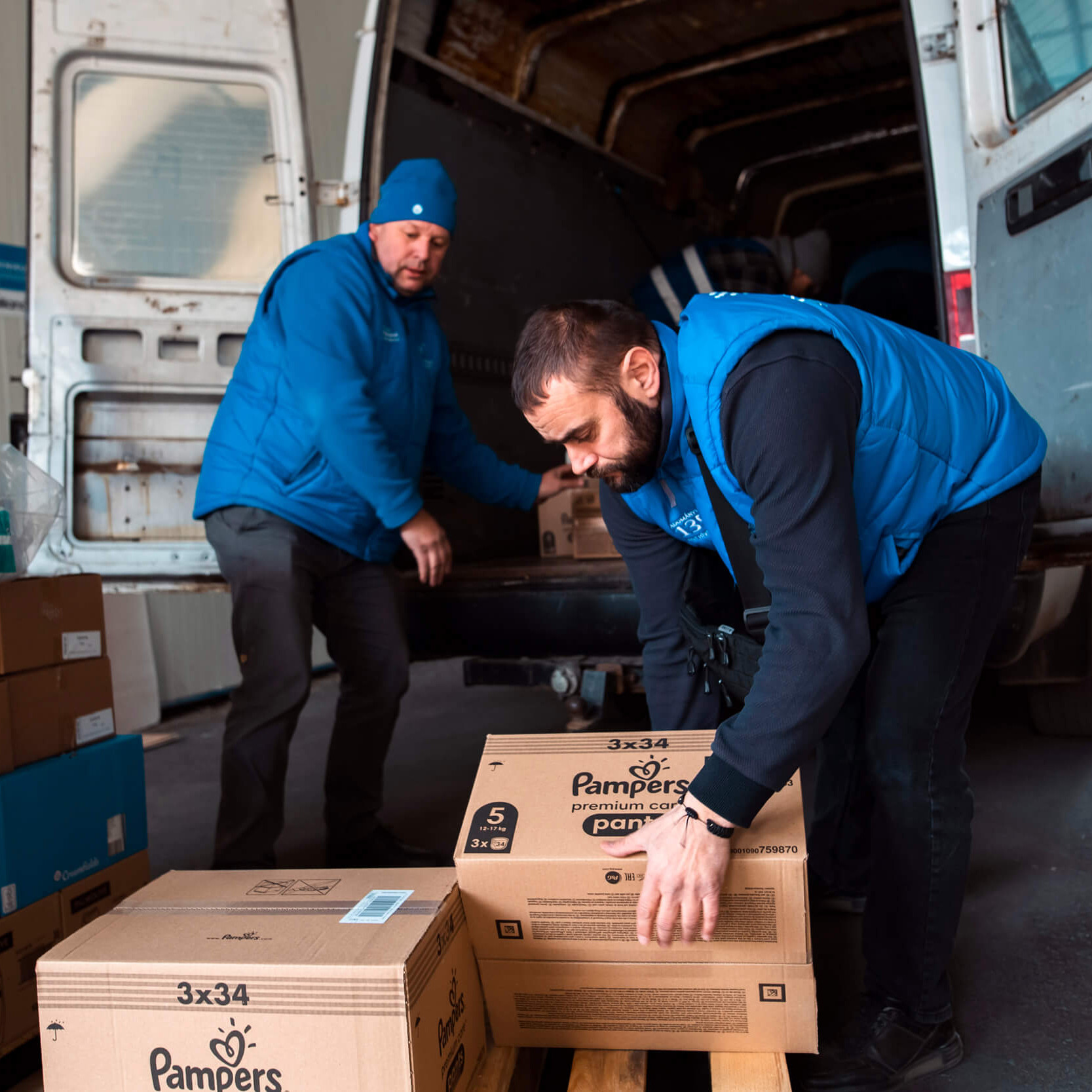 Zwei Männer laden Schachteln mit Windlen aus einem kleinen Bus aus.