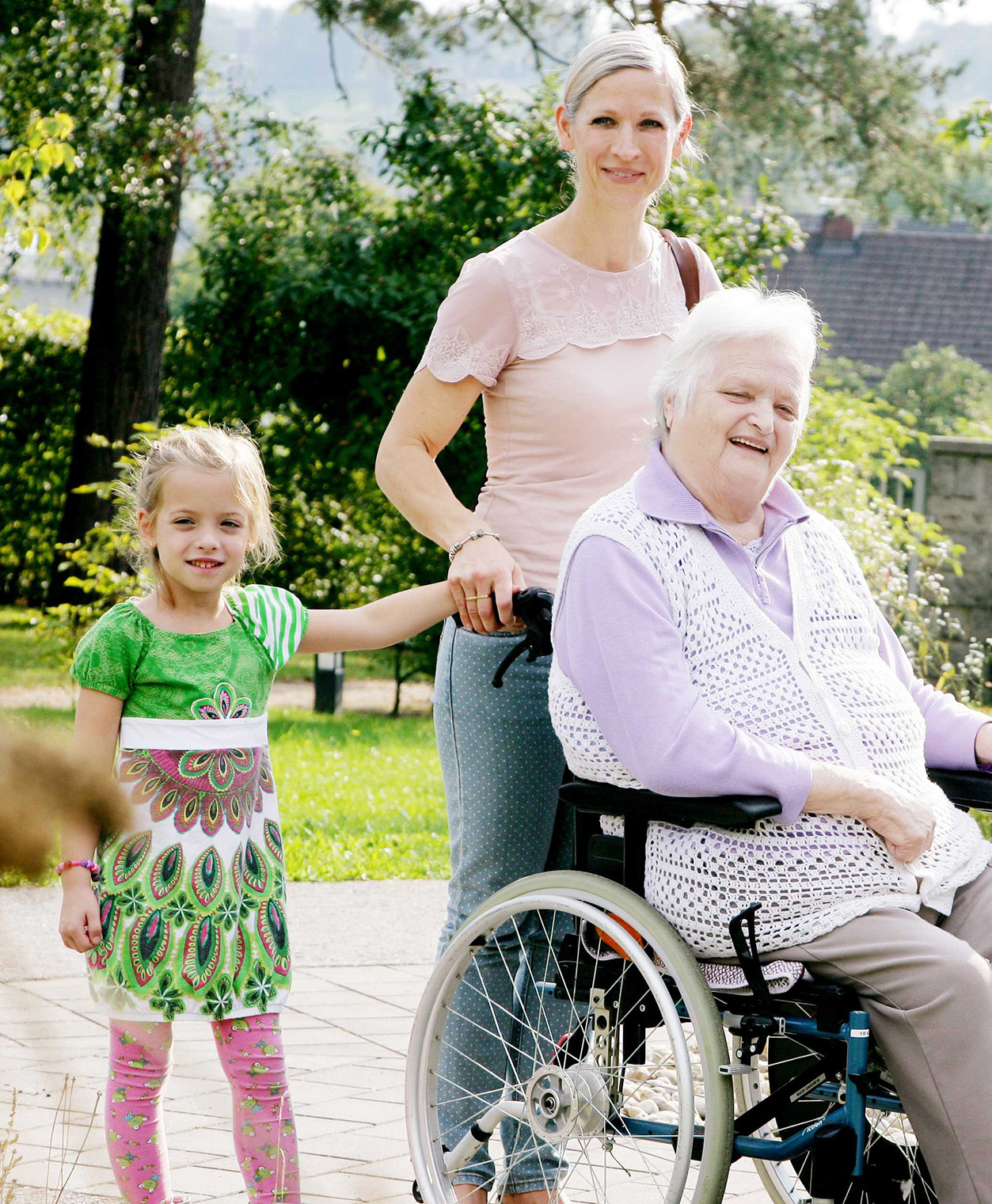 Eine ältere Frau im Rollstuhl, eine junge Frau und zwei Kinder in einem Garten.