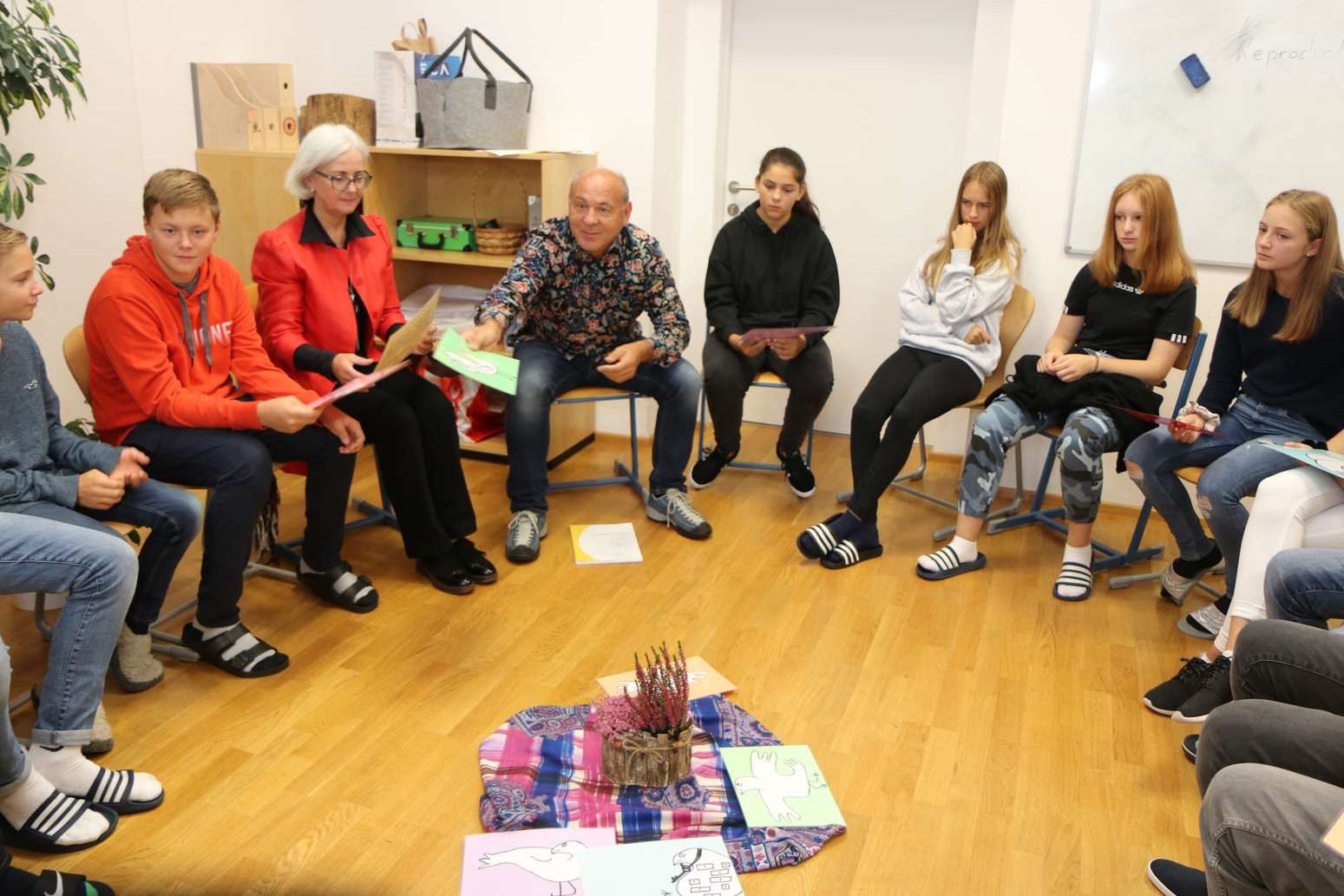 Schüler:innen sitzen im Sesselkreis in einer Klasse und halten Arbeitsblätter in den Händen.