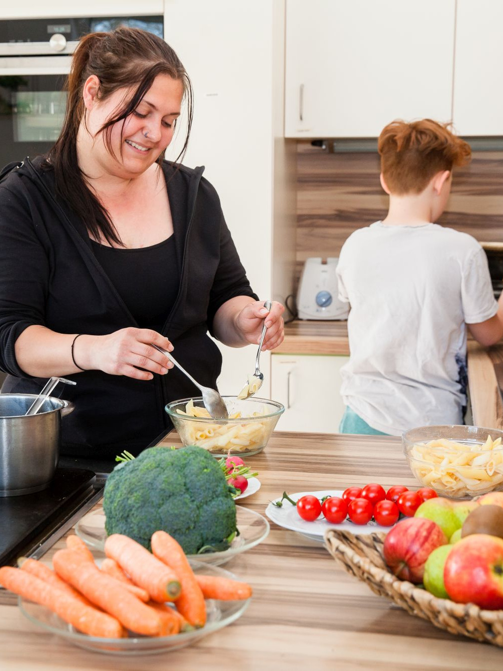 Frau steht mit Kind in der Küche, beide kochen gemeinsam
