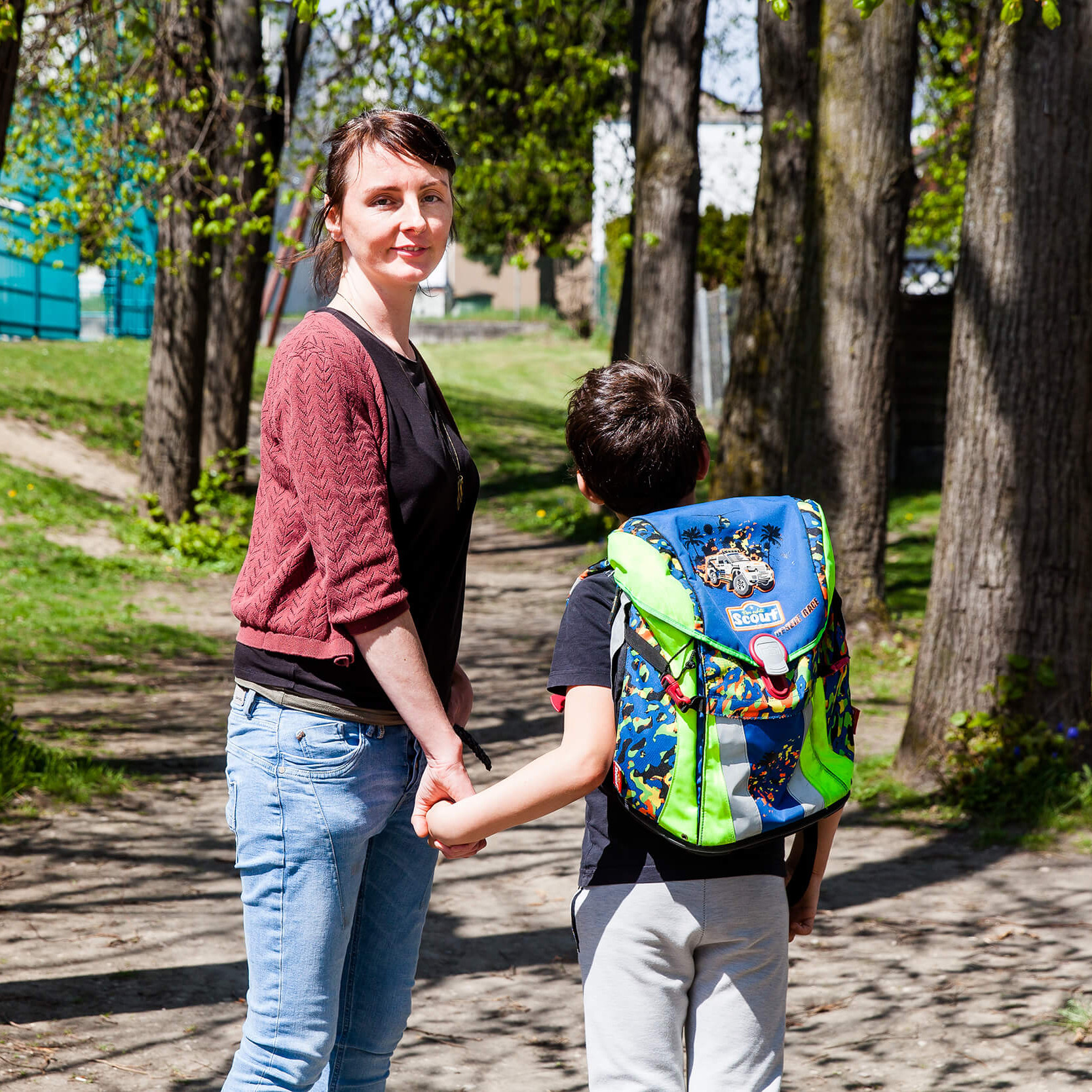 Ein Kind mit Schultasche und eine Frau auf einem Weg