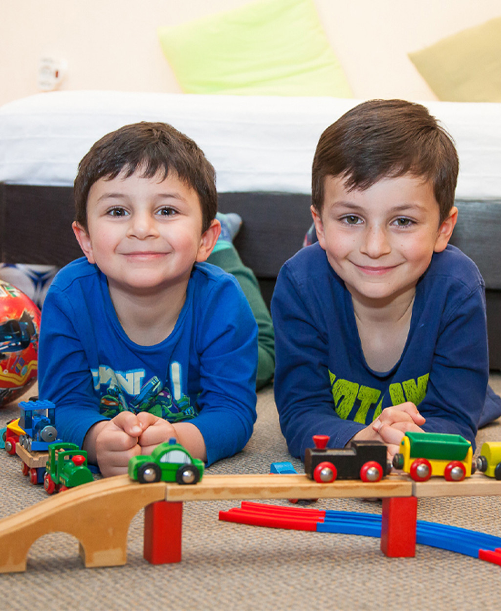 Zwei Kinder spielen mit einem Holzzug auf dem Teppich.