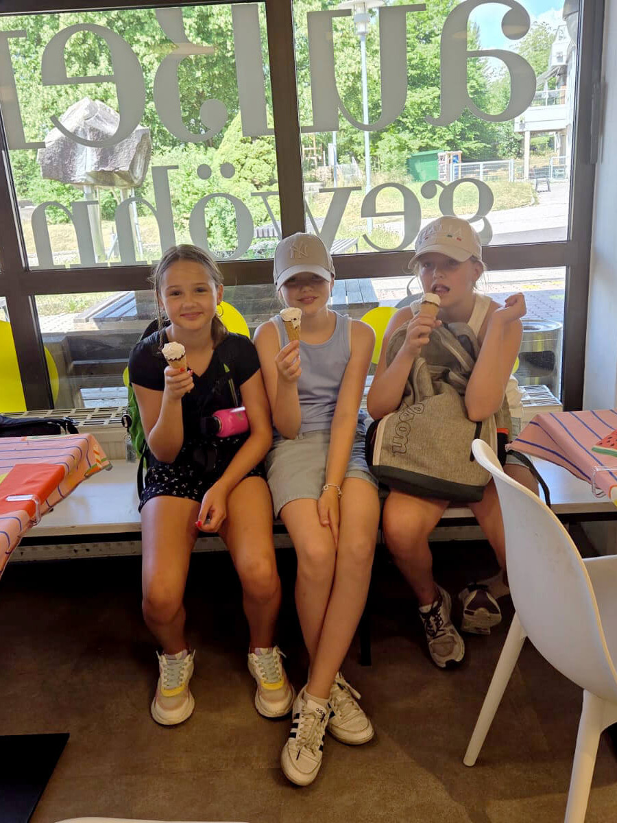 Drei Kinder sitzen auf einer Bank und essen ein Eis.