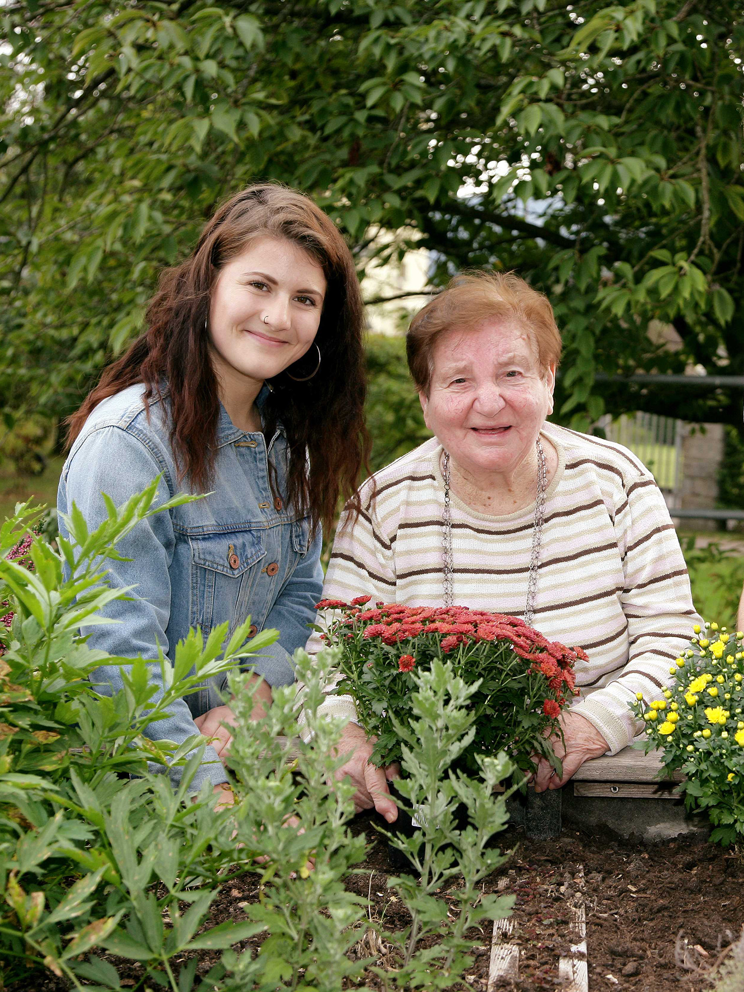 Zwei junge Menschen und eine Frau im Alter setzen gemeinsam Blumen in ein Hochbeet.