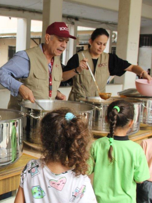 Ein Mann und eine Frau geben Kindern aus großen Kochtöpfen warmes Essen in Schüsseln