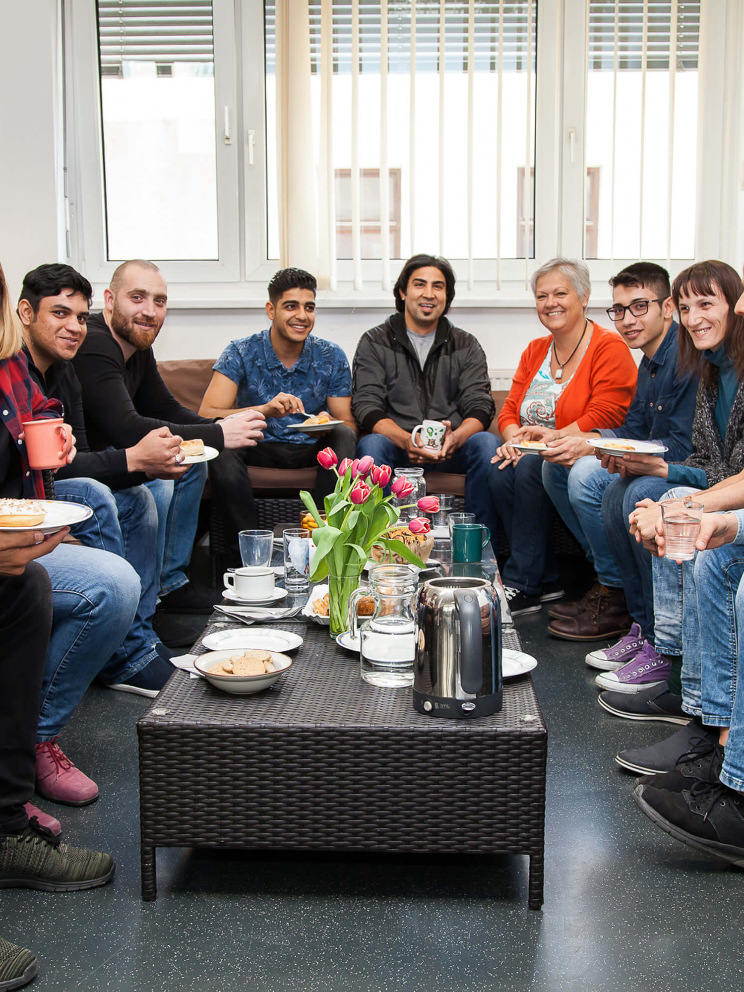 Eine gruppe von Menschen sitzt bei Kaffee und Kuchen um einen Tisch.