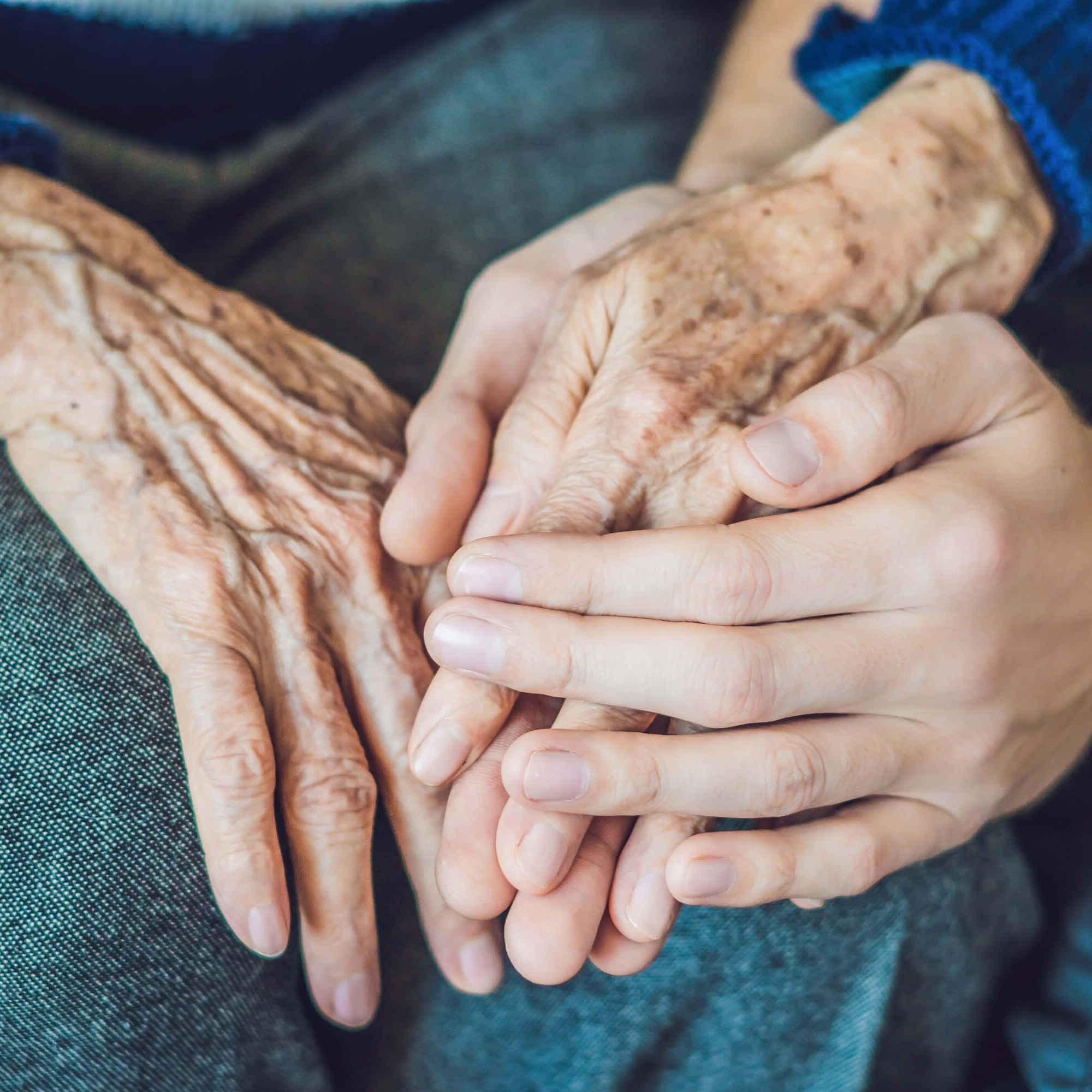 Hände eines jüngeren Menschen halten die Hände eines älteren Menschen.