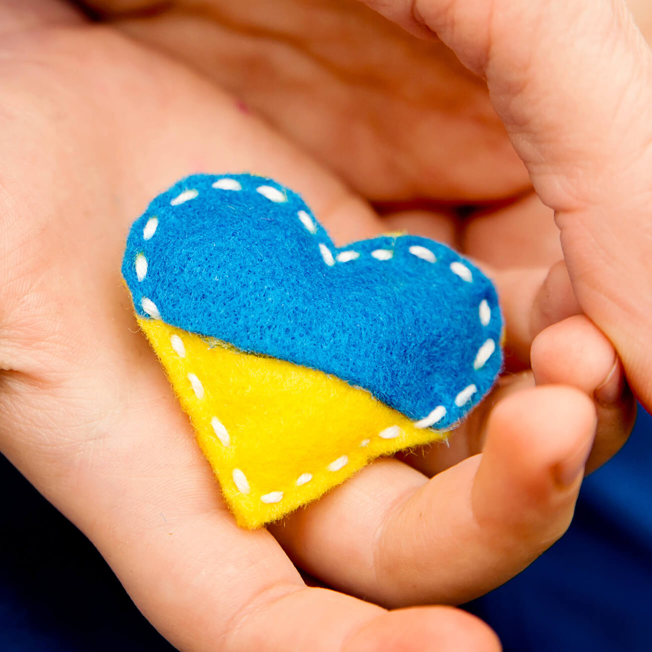 Eine Kinderhand hält ein Filzherzchen in den Farben der Flagge der Ukraine.