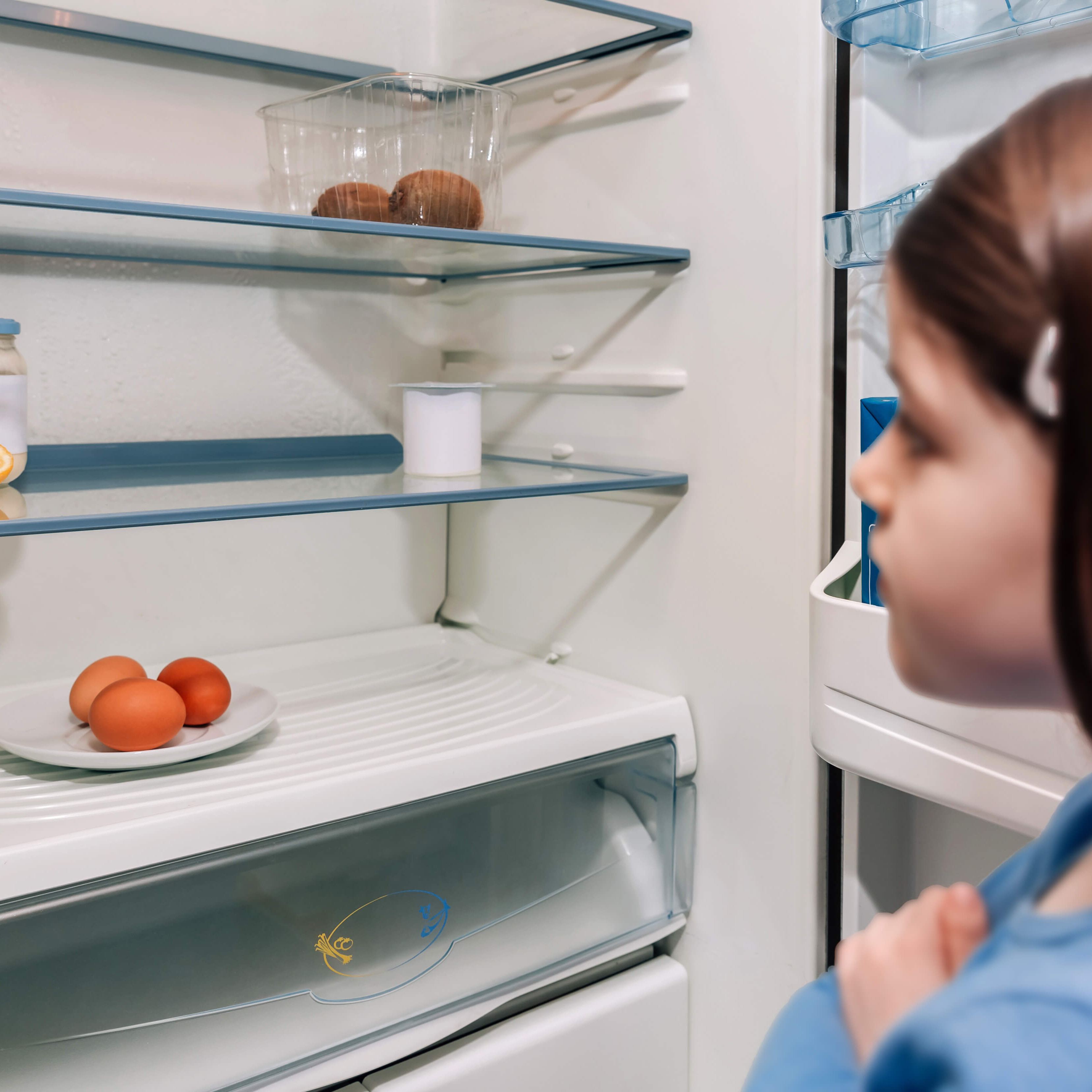 Ein Mädchens steht vor einem fast leeren Kühlschrank