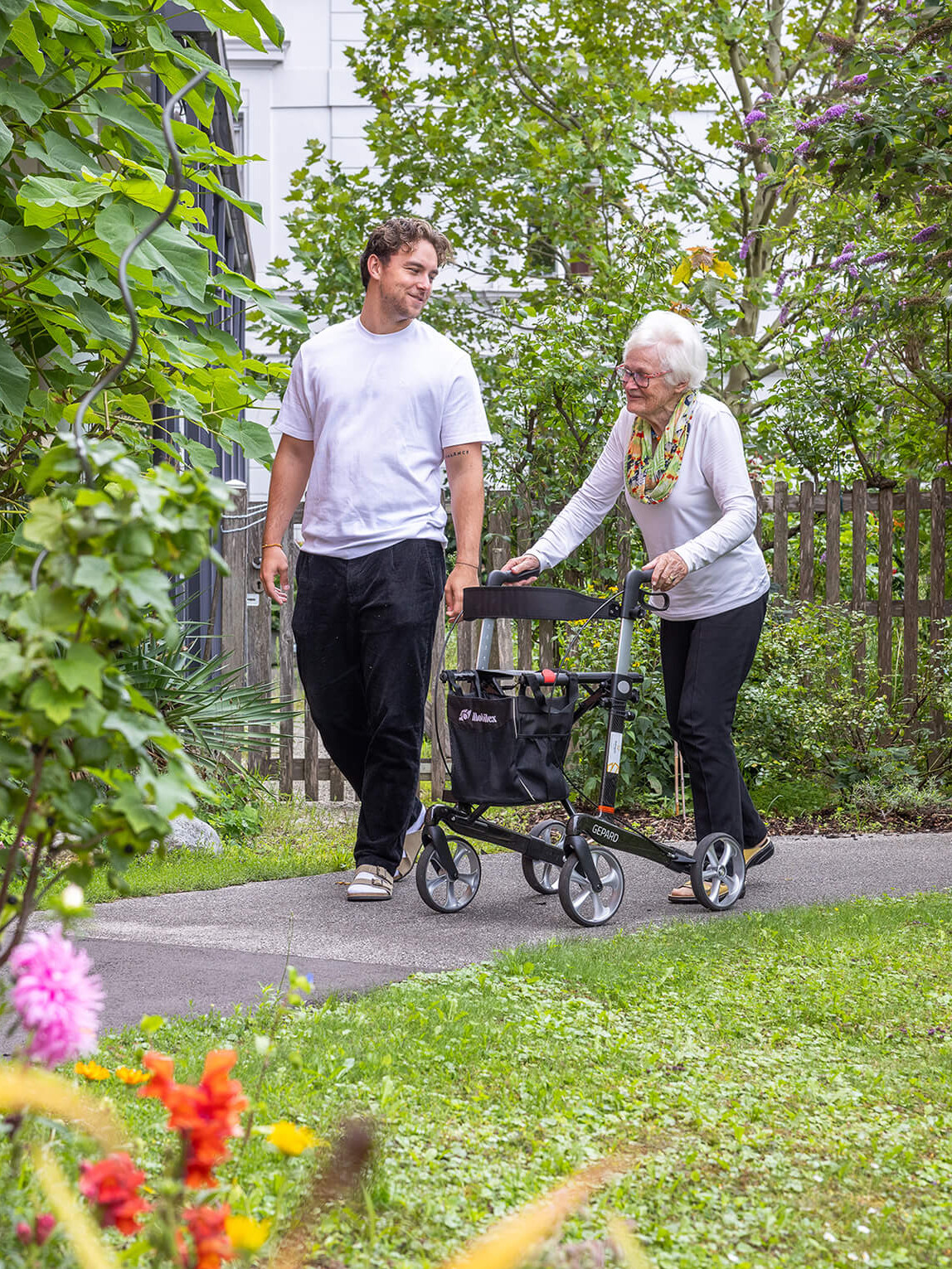 Ein junger Mann und eine alte Frau spazieren in einem Garten.