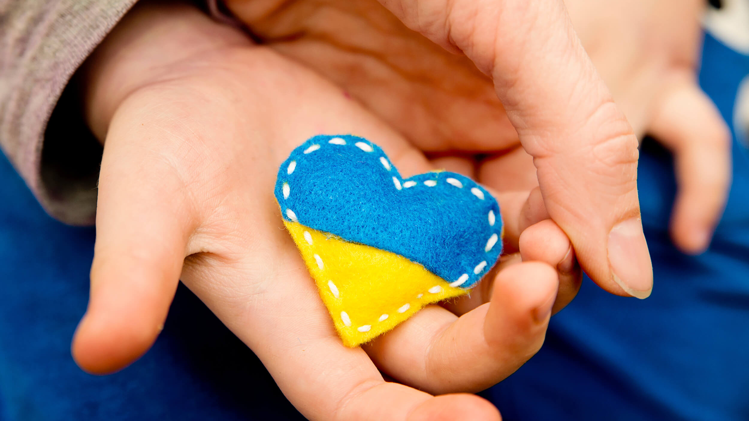 Eine Kinderhand hält ein Filzherzchen in den Farben der Flagge der Ukraine.