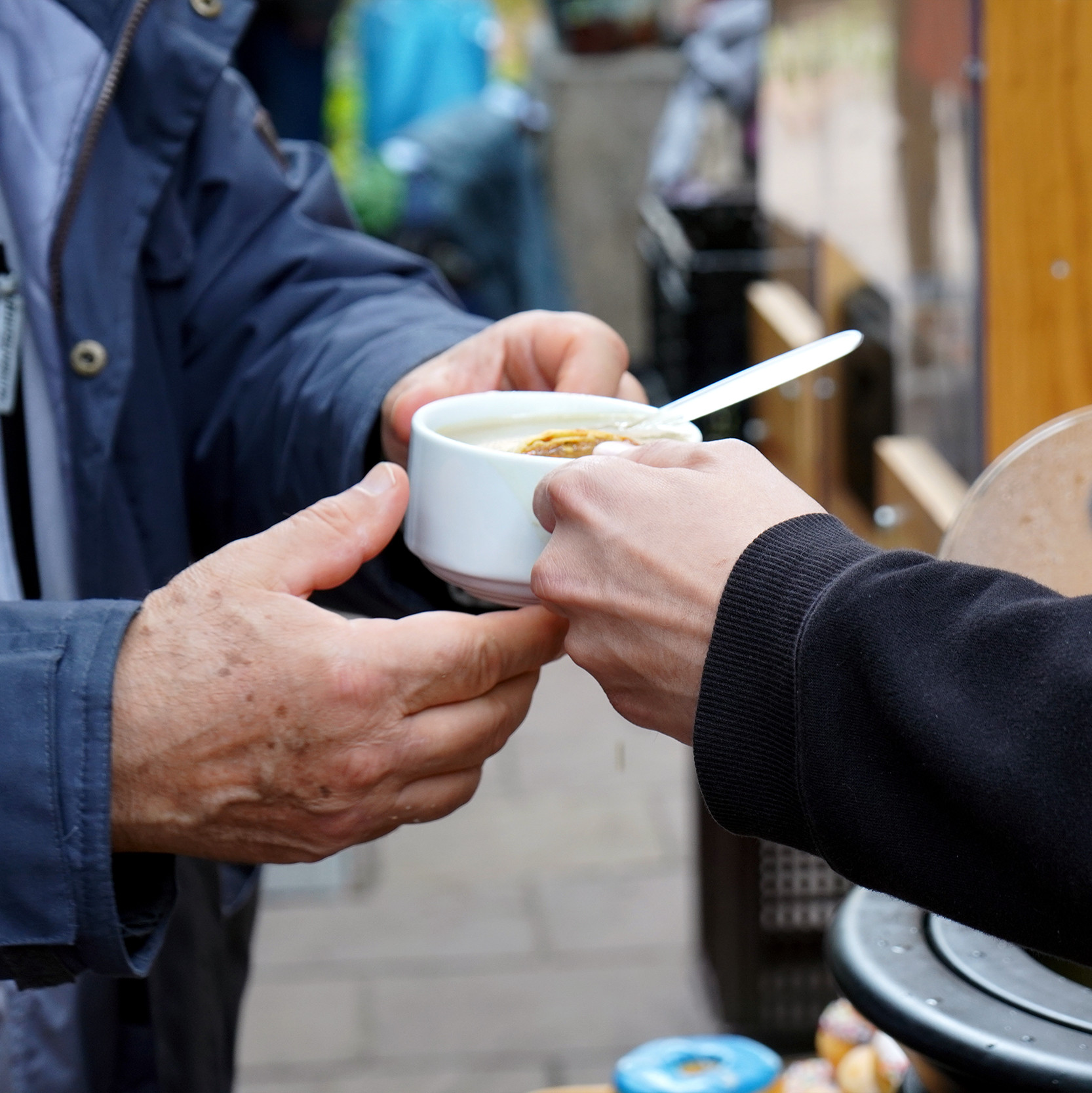 Ein Mitarbeiter im 's Häferl der Diakonie überreicht einem Gast draußen eine warme Suppe