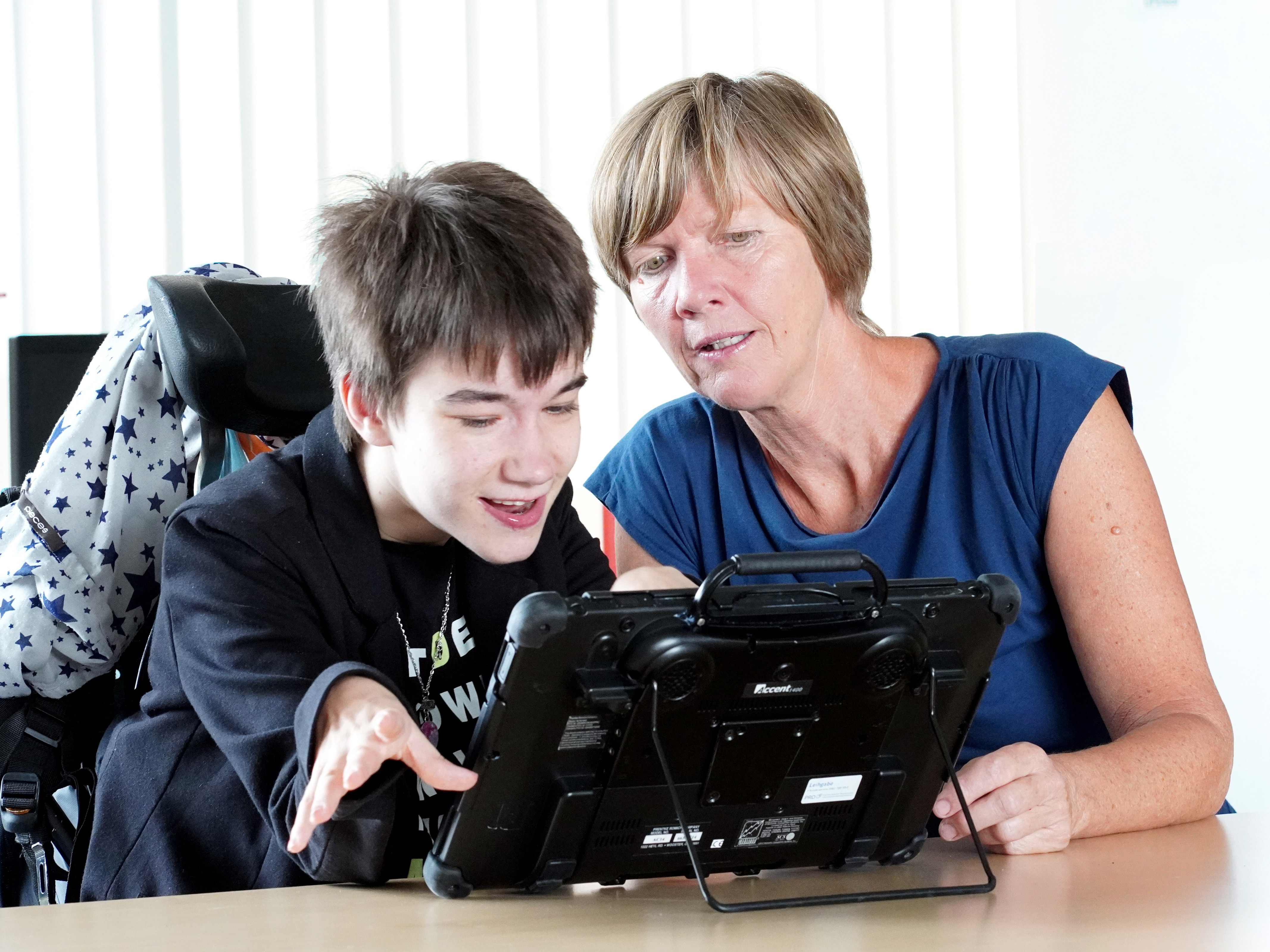 Eine junge Frau mit Sprachcomputer und eine Mitarbeiterin der Diakonie unterhalten sich.