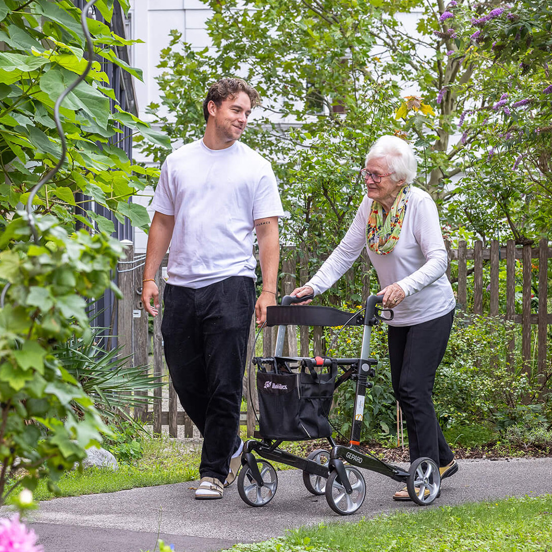 Ein junger Mann und eine alte Frau spazieren in einem Garten.