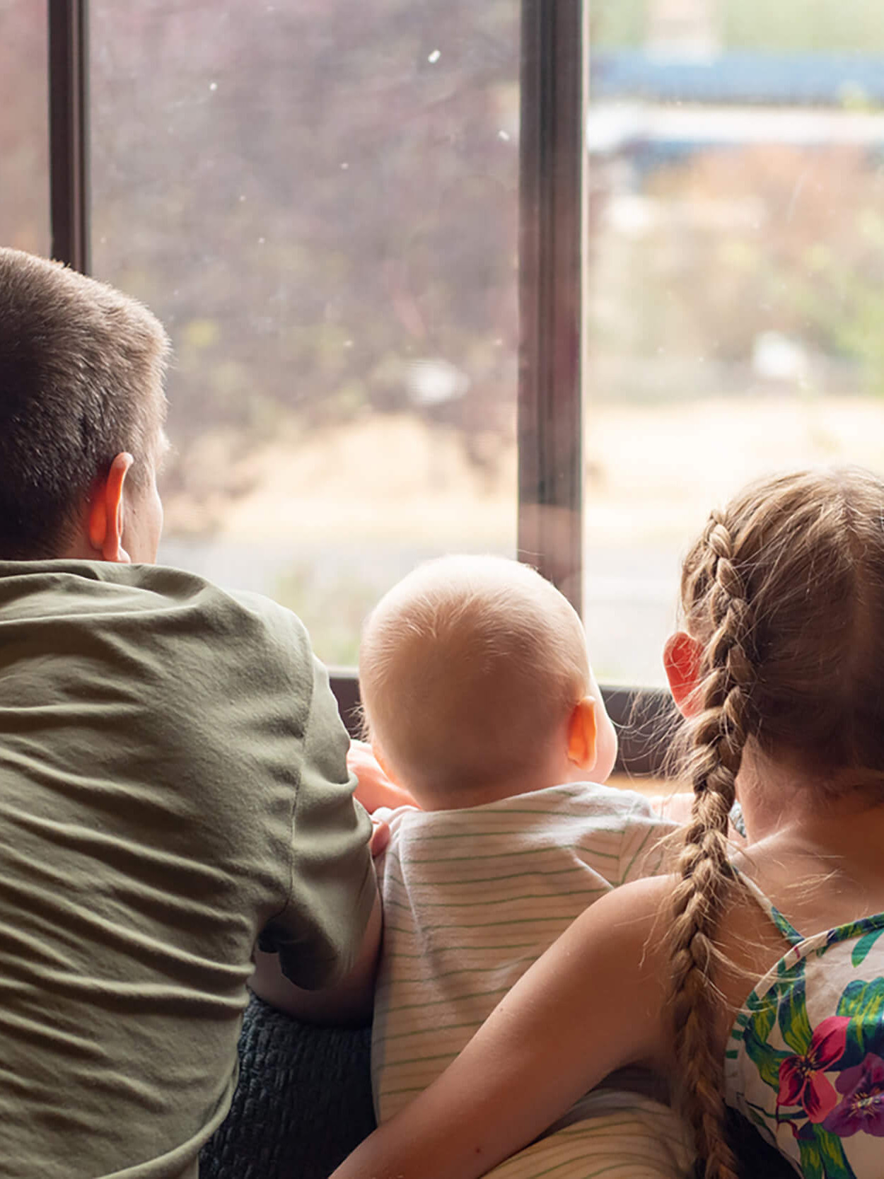 Drei Kinder schauen aus einem Fenster.