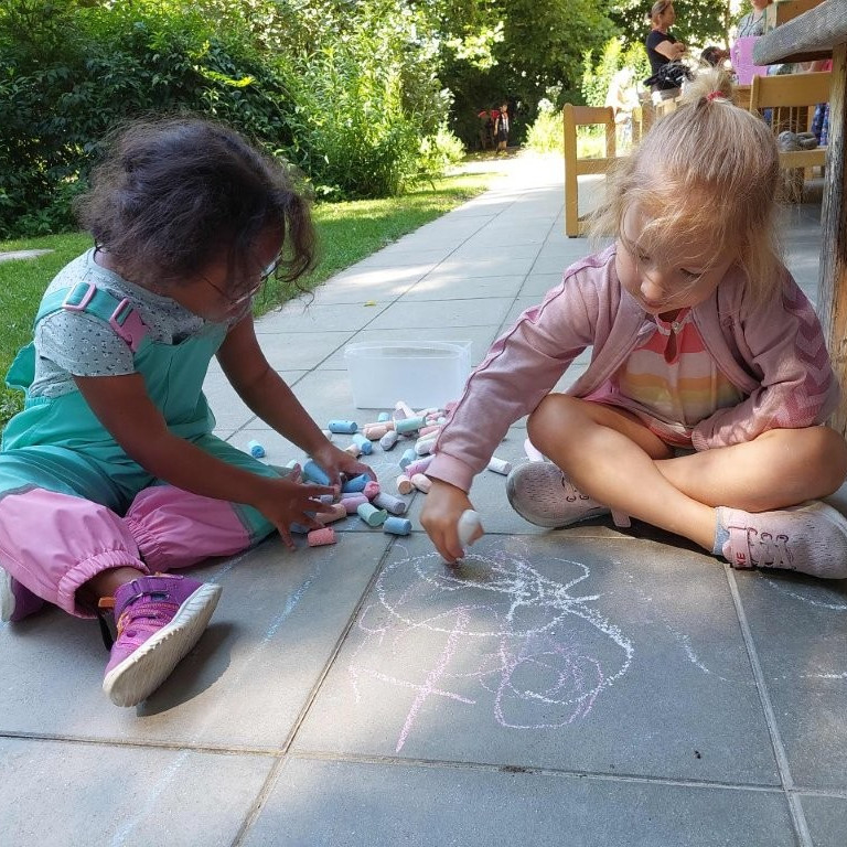 Zwei Mädchen spielen zusammen mit Straßenkreide