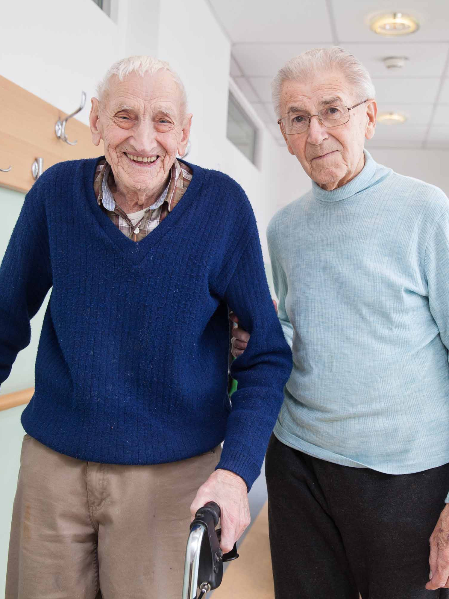 Ein Mann im Rollator wird von einem angehörigen begleitet.