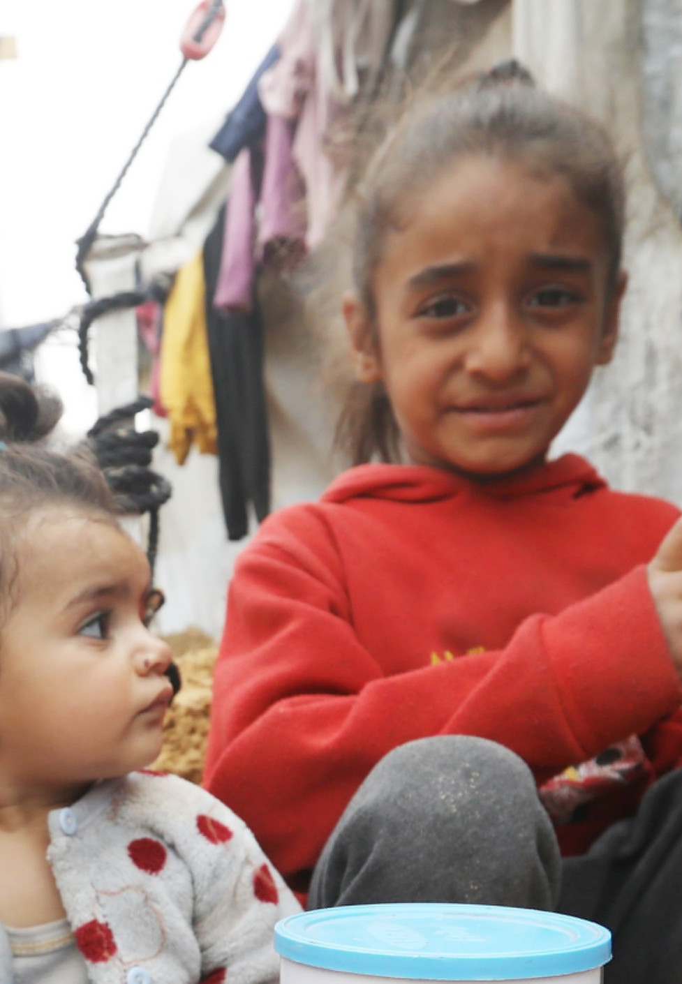 Kinder sitzen in Zeltlager auf dem Sandboden.