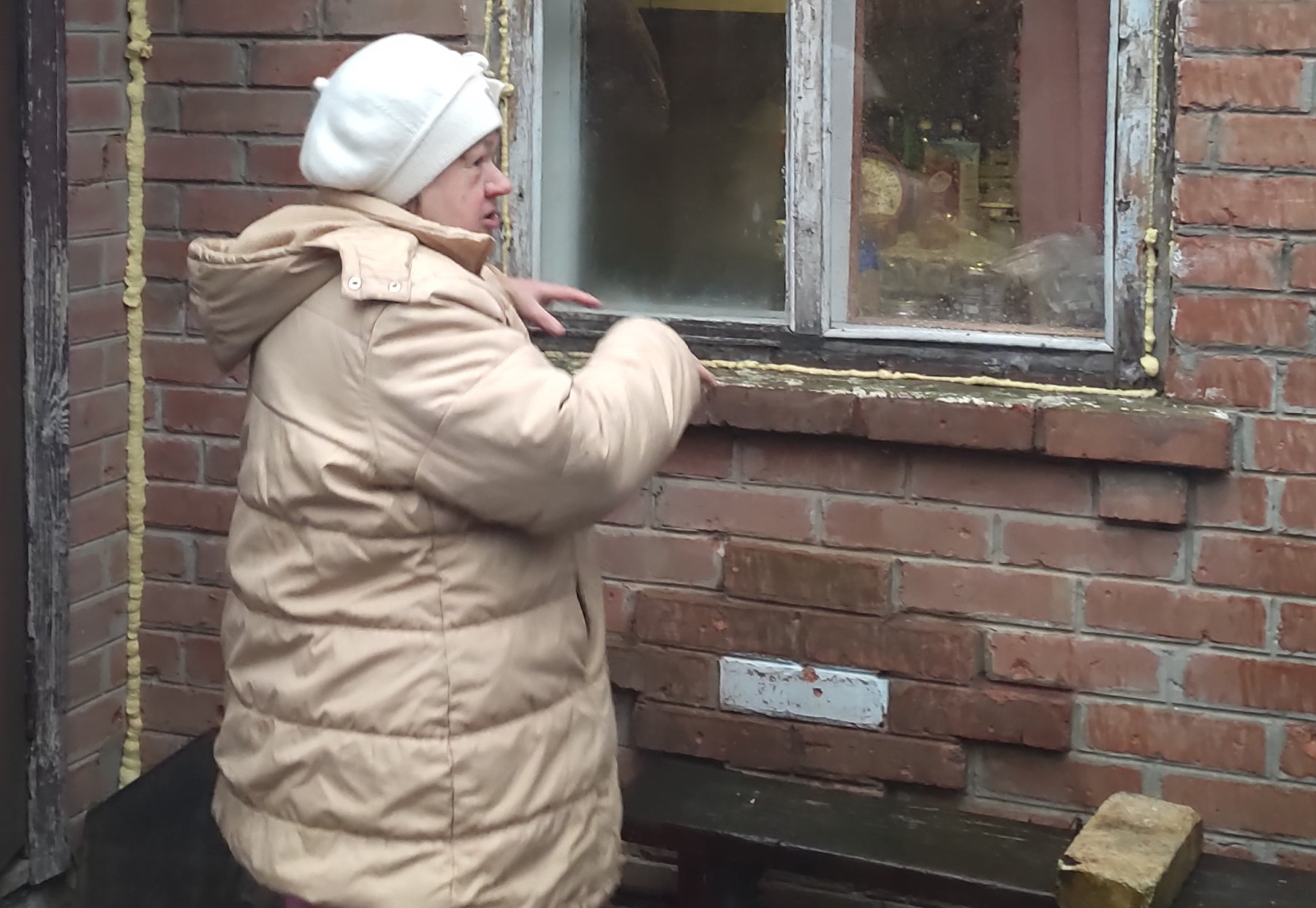 Eine Frau vor einem Hauseingang eines unverputzten und notdürftig reparierten Hauses.