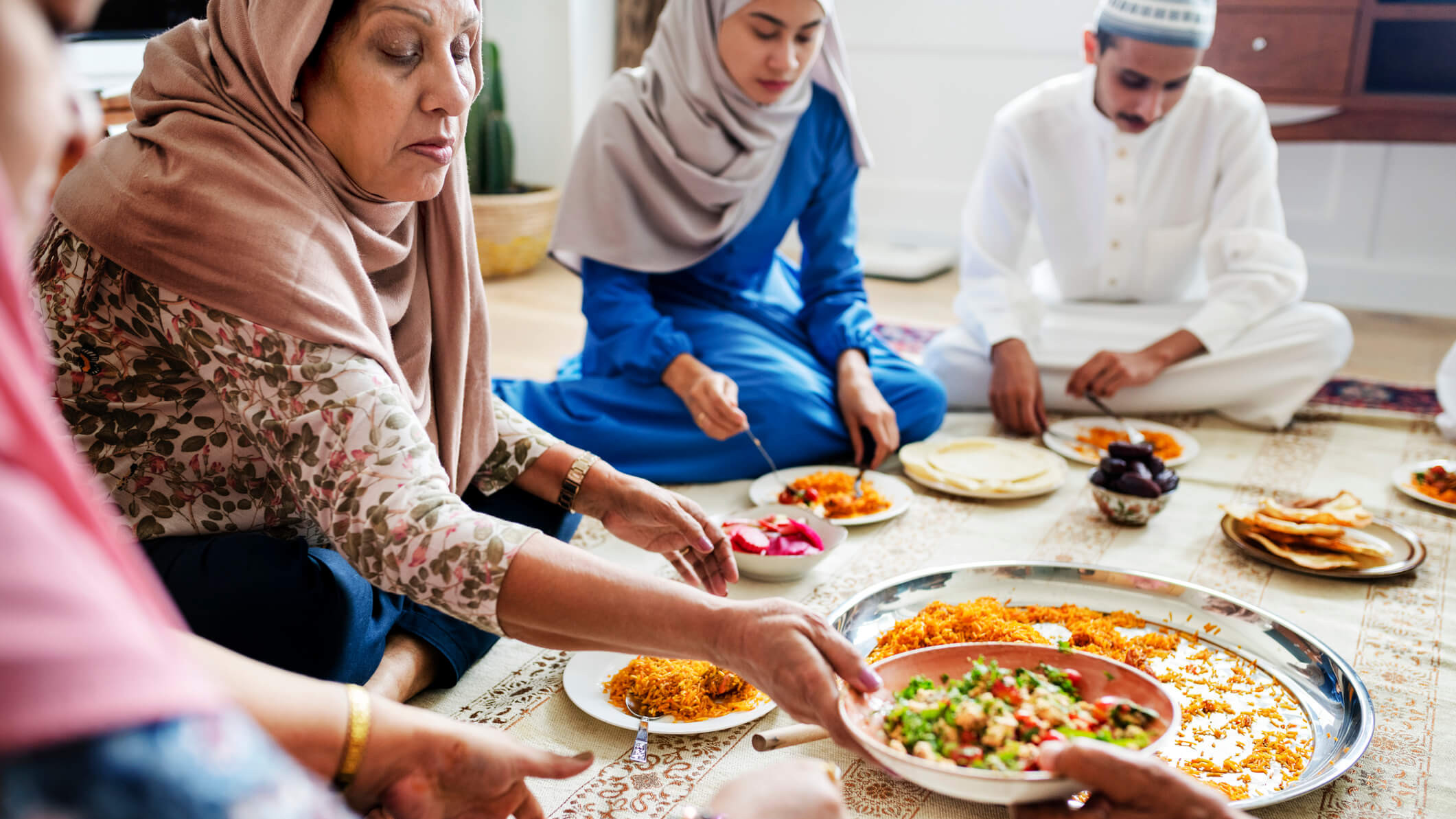 Familie sitzt auf dem Boden und teilt eine gemeinsame Mahlzeit.