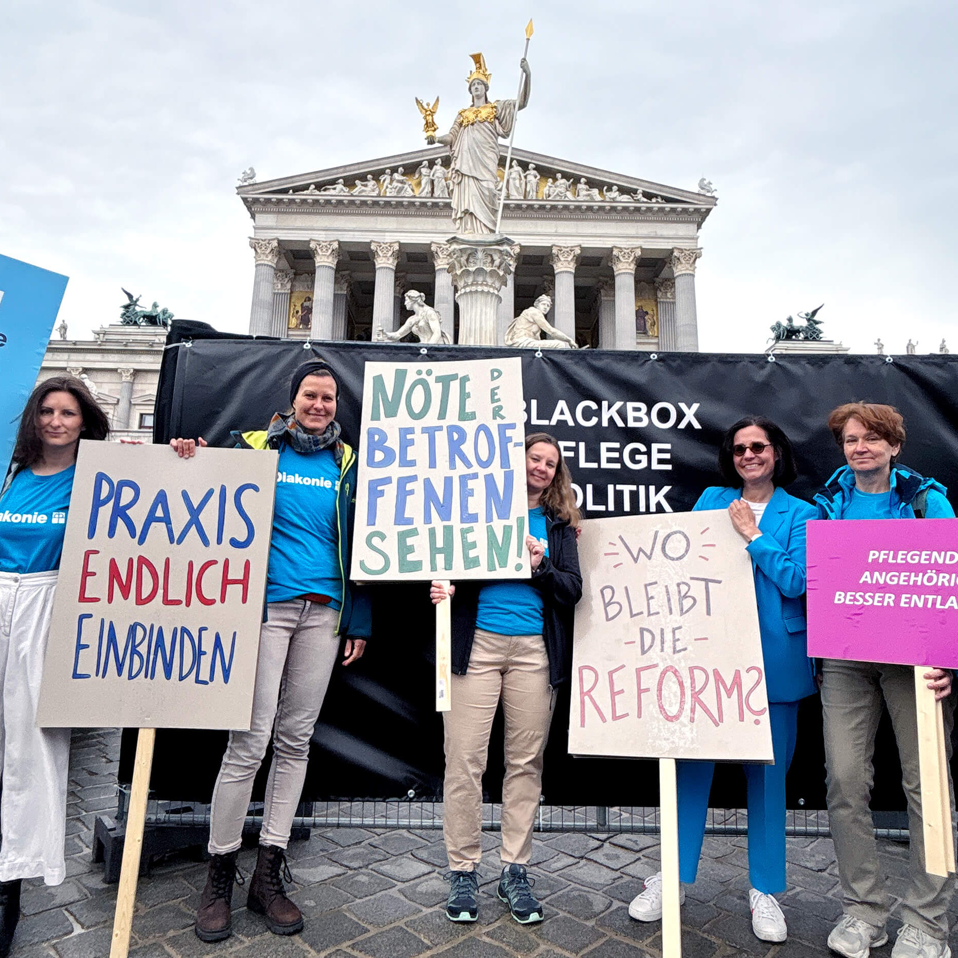 Diakonie-Mitarbeiterinnen mit Demo-Schildern vor dem Parlament