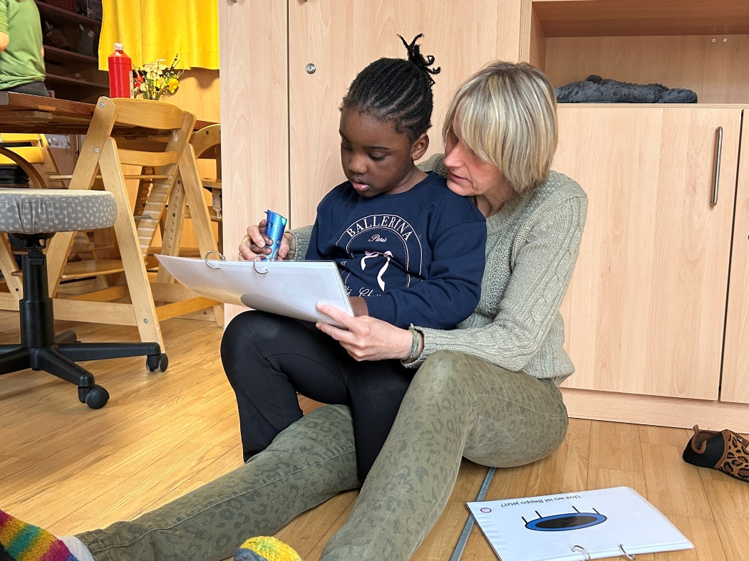 Kind sitzt auf Schoß von Dame, gemeinsam betrachten sie ein Dokument