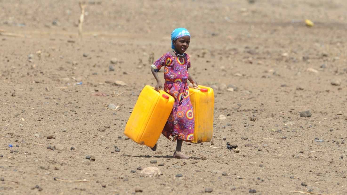Mädchen mit zwei leeren gelben Wasserkanistern in einer von Dürre betroffenen Landschaft. Ihre Spende gegen die Hungersnot hilft.