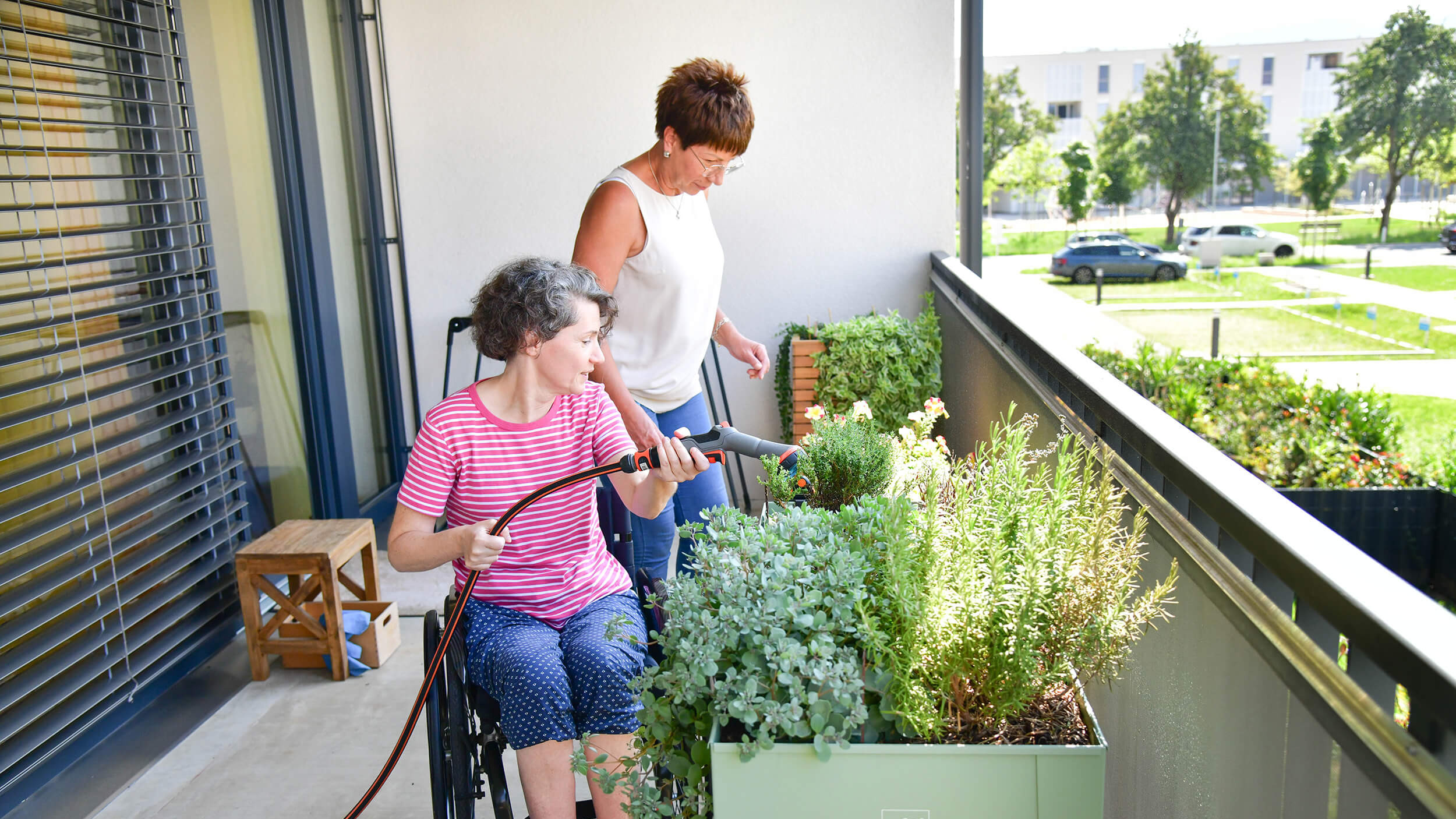 Zwei Frauen gießen Blumen am Balkon.