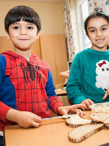 Zwei Kinder bereiten gemeinsam ein Brot mit Aufstrich zu.