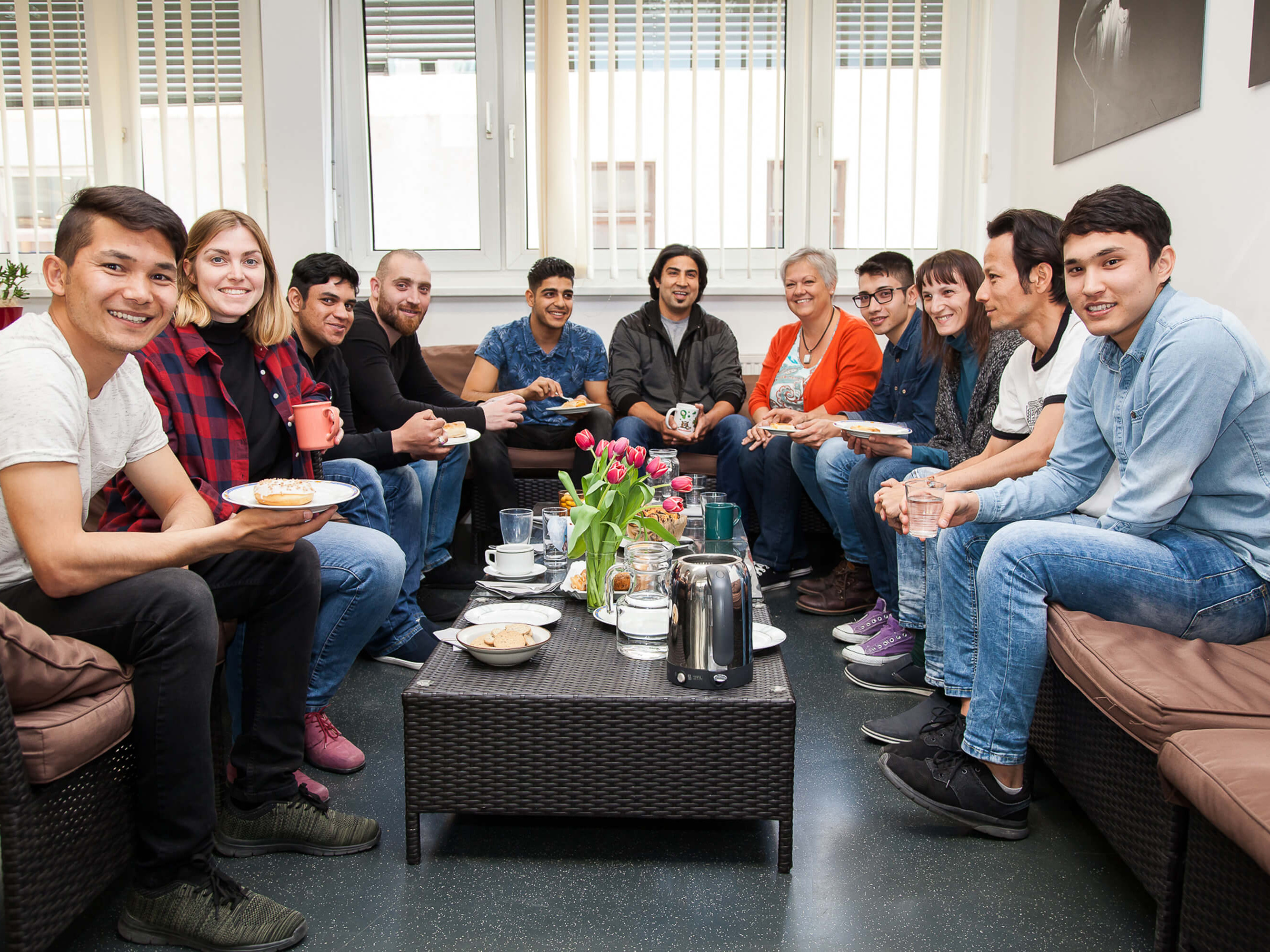 Eine gruppe von Menschen sitzt bei Kaffee und Kuchen um einen Tisch.