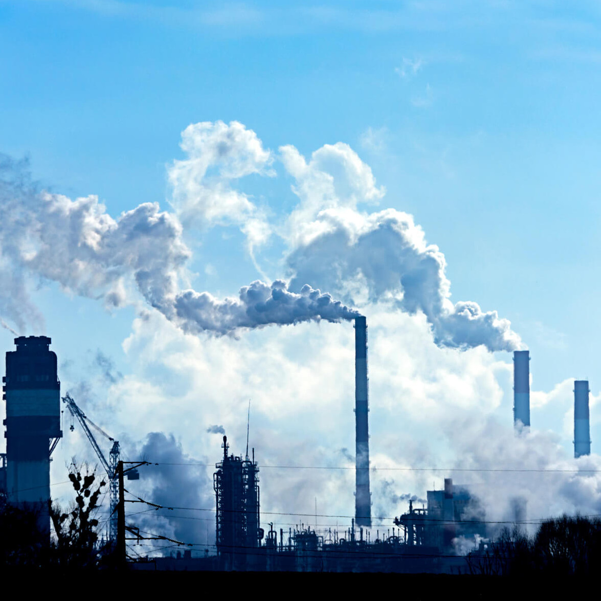 Farbikschornsteine mit viel Rauch vor blauem Himmel.