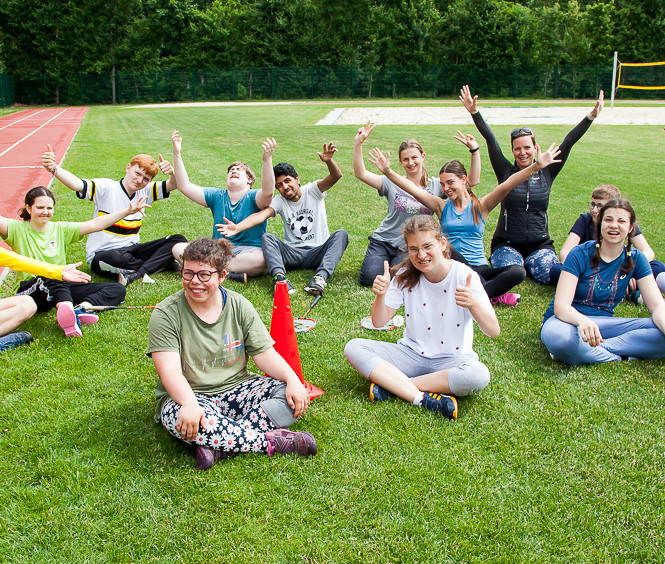 Eine Gruppe Schüler:innen sitzen am Rasen eines Sportplatzes und jubeln