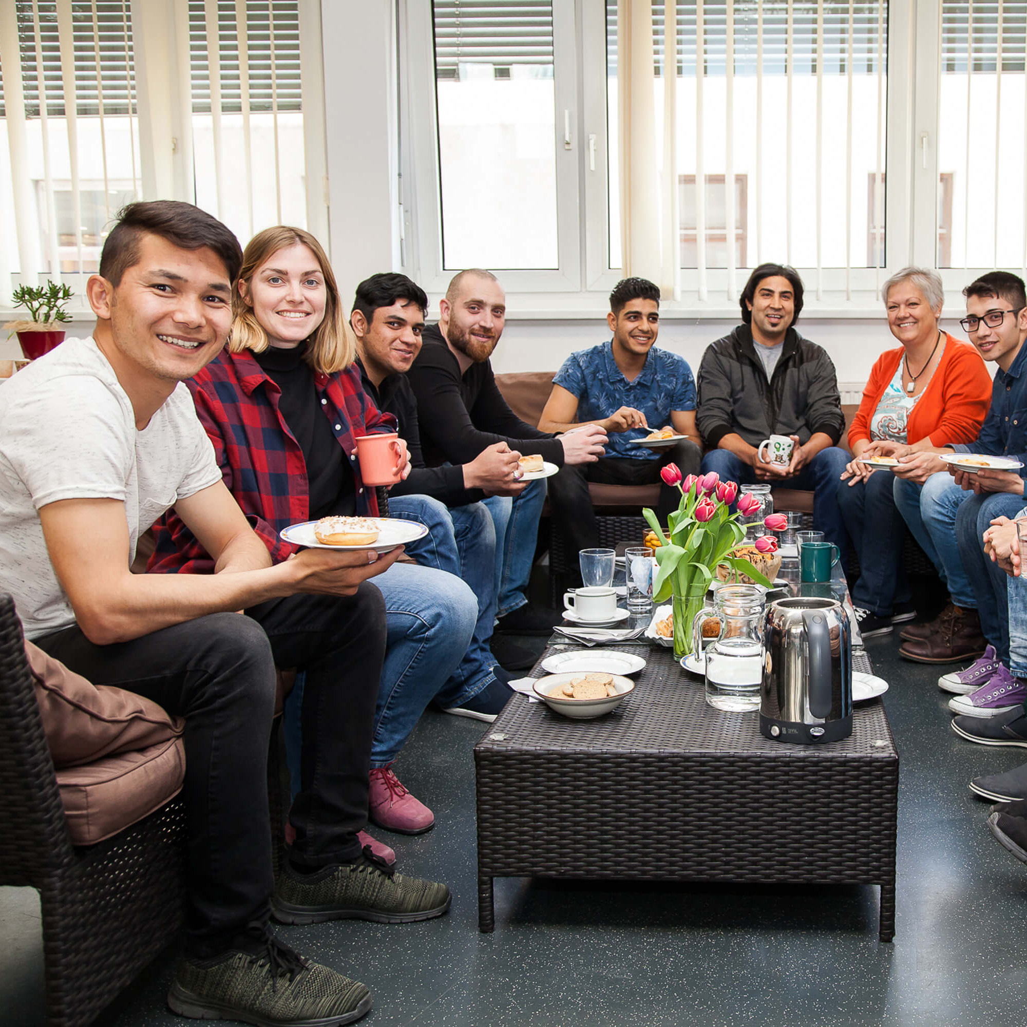 Eine gruppe von Menschen sitzt bei Kaffee und Kuchen um einen Tisch.