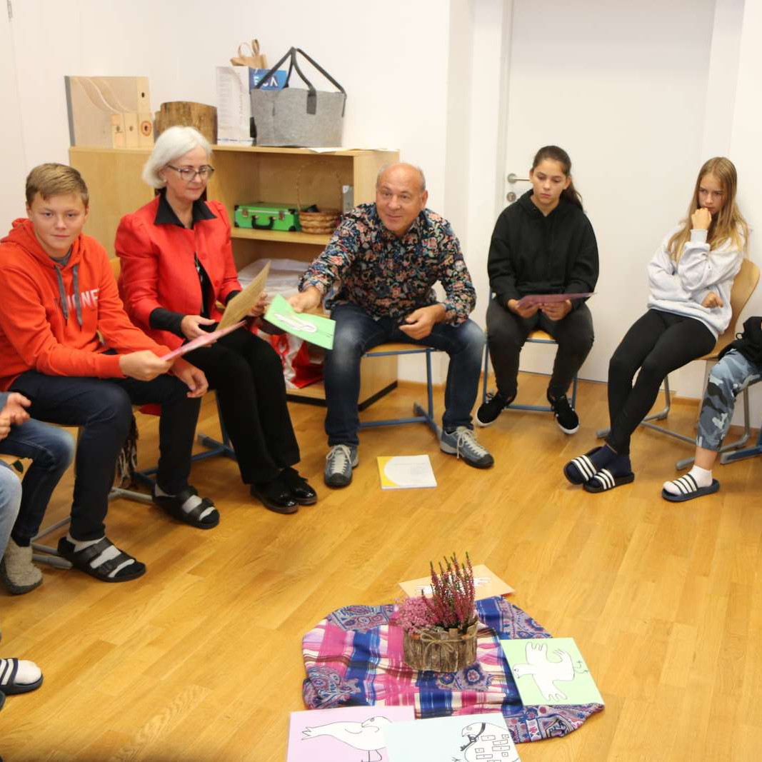 Schüler:innen sitzen im Sesselkreis in einer Klasse und halten Arbeitsblätter in den Händen.