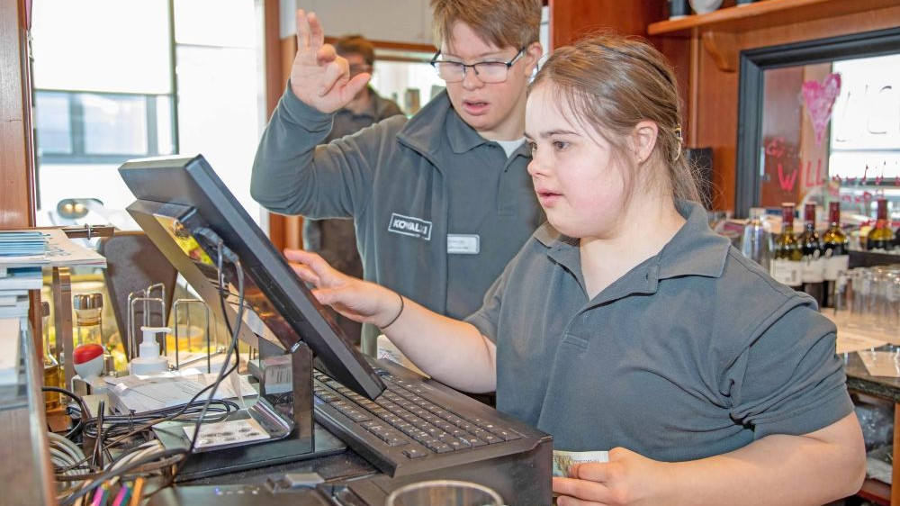 Junge Frau arbeitet mit Kollege an der Kasse in einem Cafe