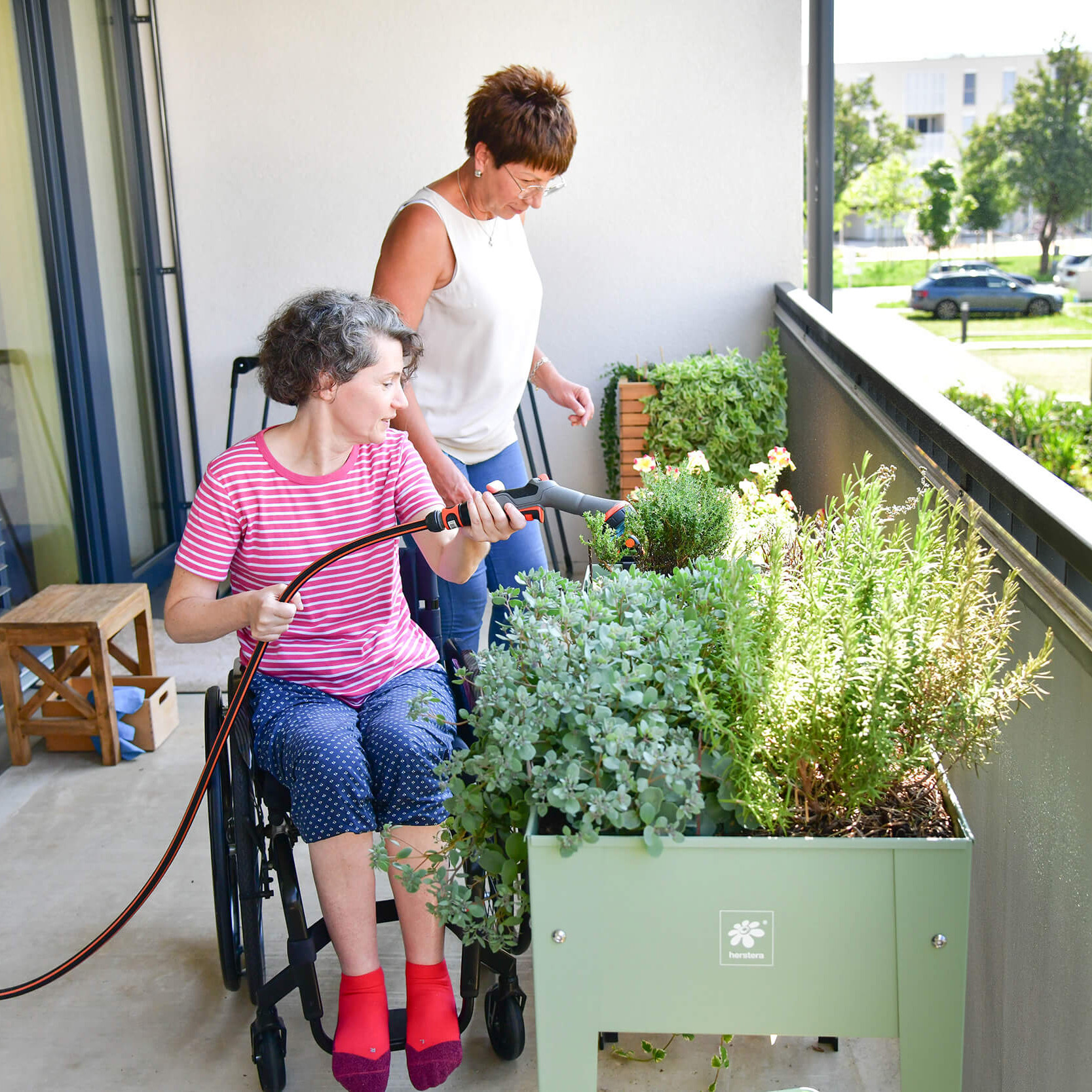 Zwei Frauen gießen Blumen am Balkon.