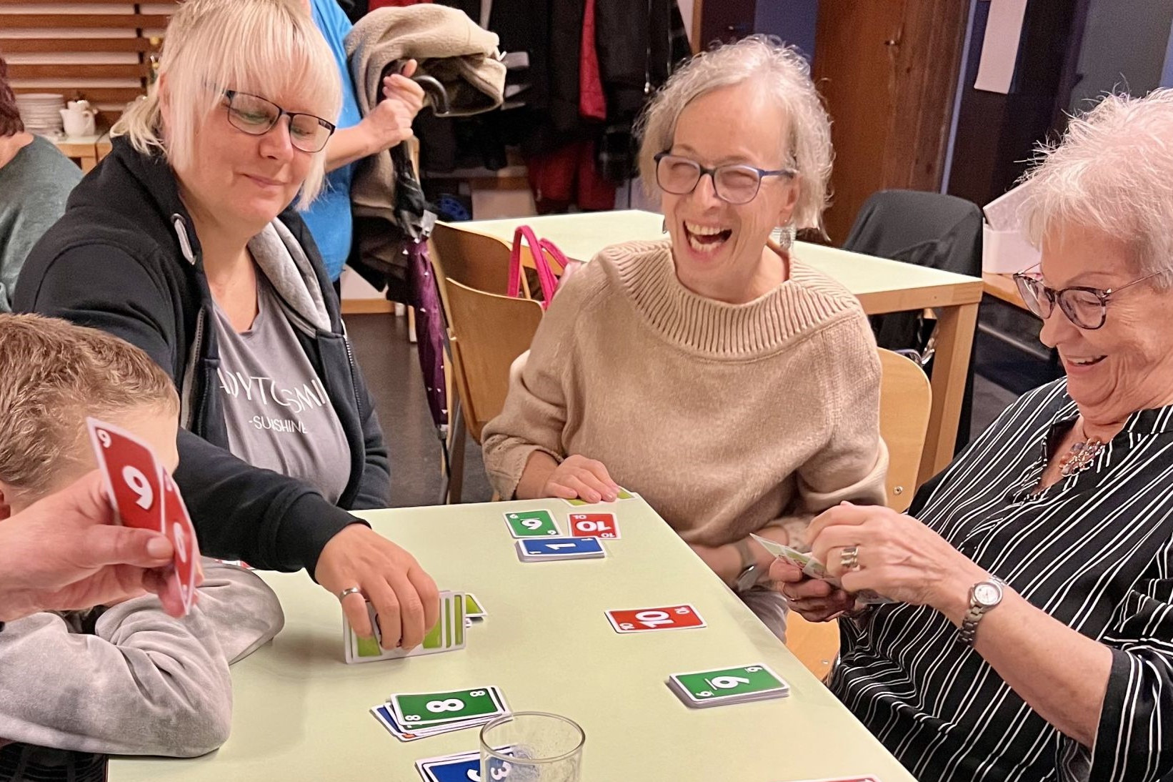 Drei Frauen und ein Bub sitzen an einem Tisch und spielen Uno