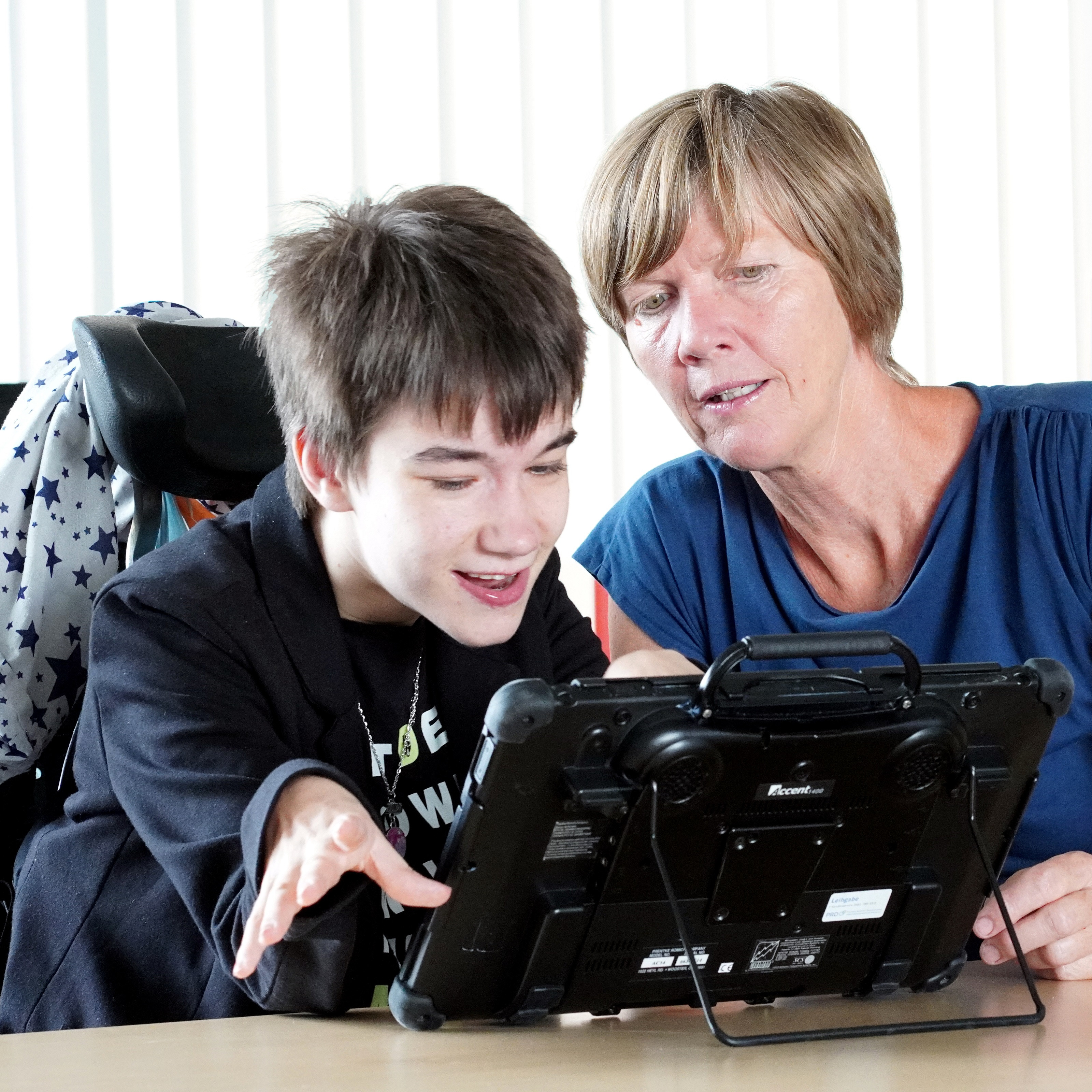 Eine junge Frau mit Sprachcomputer und eine Mitarbeiterin der Diakonie unterhalten sich.