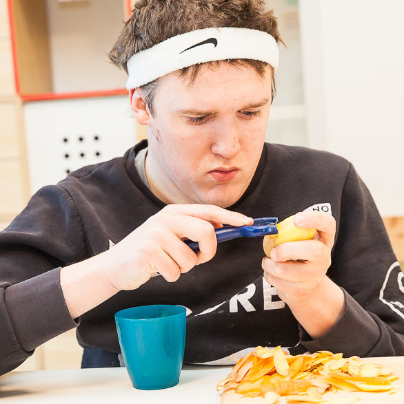 Mann sitzt bei Tisch und schält Kartoffel