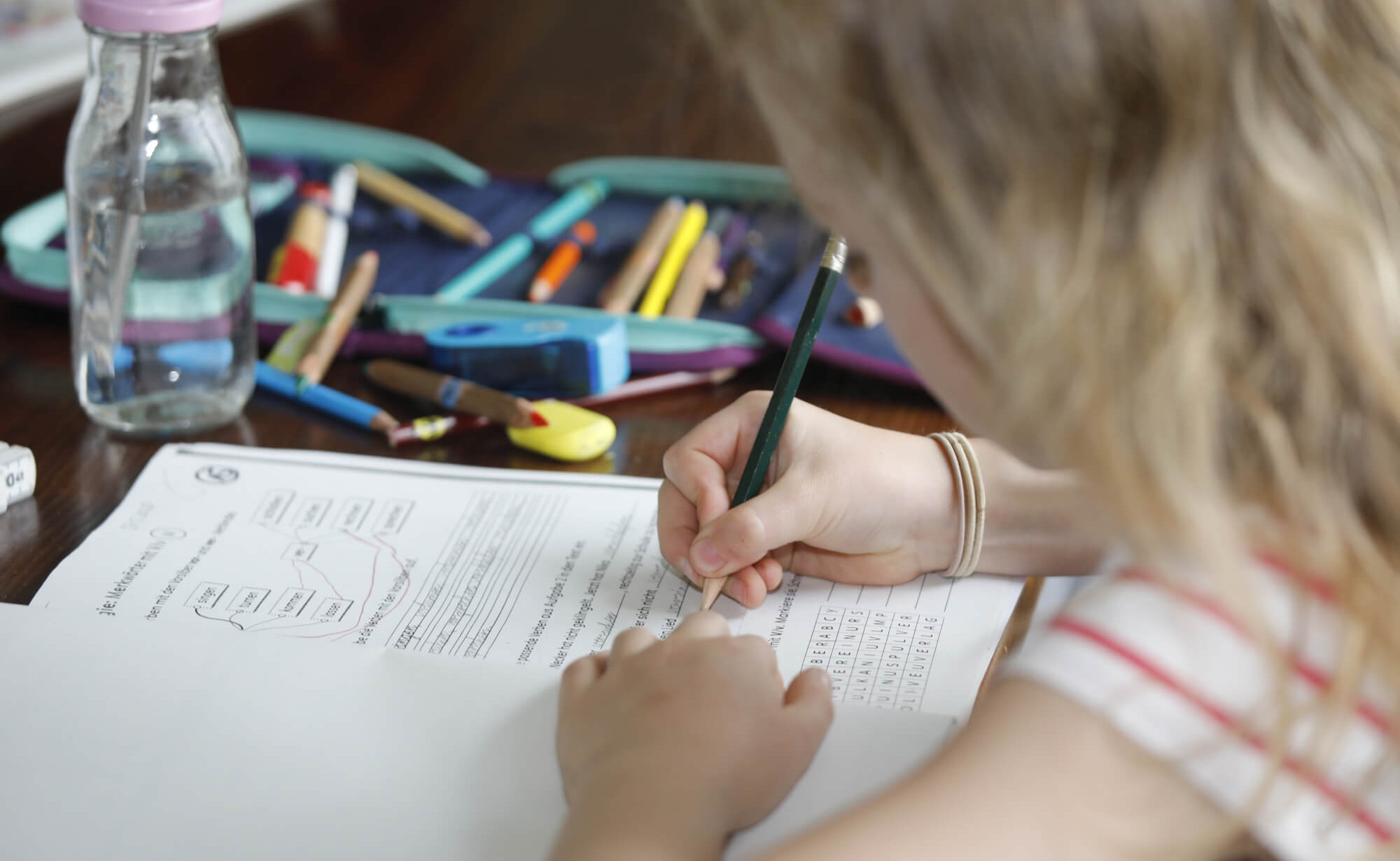 Mädchen sitzt an einem Tisch und schreibt mit Bleistift auf ein Arbeitsblatt